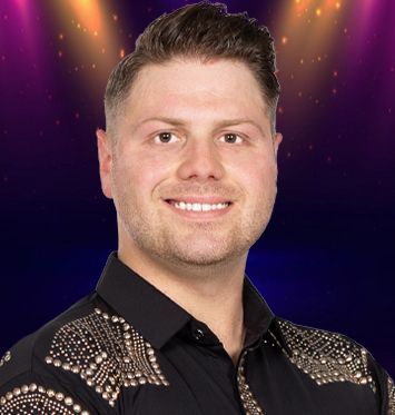 A man in a black shirt with gold studs on the sleeves is smiling for the camera.