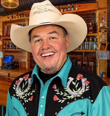 A man wearing a cowboy hat and a blue shirt with horseshoes on it