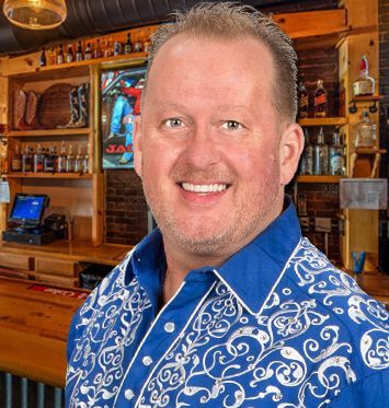 A man in a blue and white shirt is smiling in front of a bar.