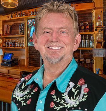 A man wearing a horseshoe vest is smiling in a bar