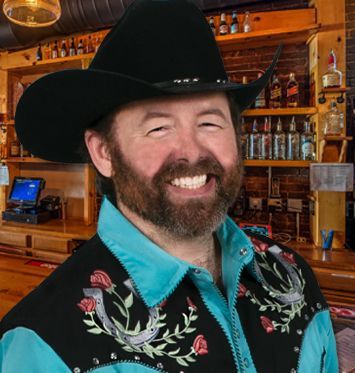 A man wearing a cowboy hat and a vest with horseshoes on it