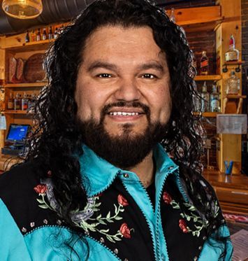 A man with long hair and a beard is wearing a blue and black jacket