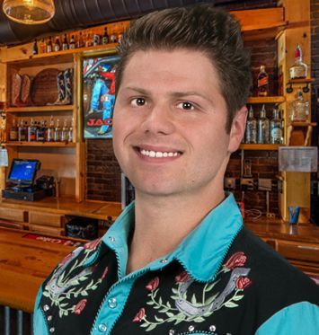 A man in a blue shirt is smiling in front of a bar