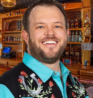 A man with a beard is smiling in front of a bar