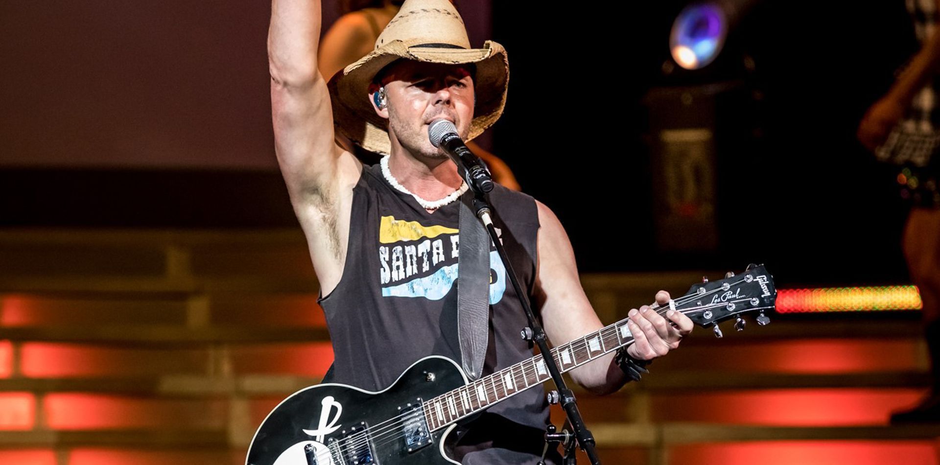 A man in a cowboy hat is singing into a microphone while holding a guitar.