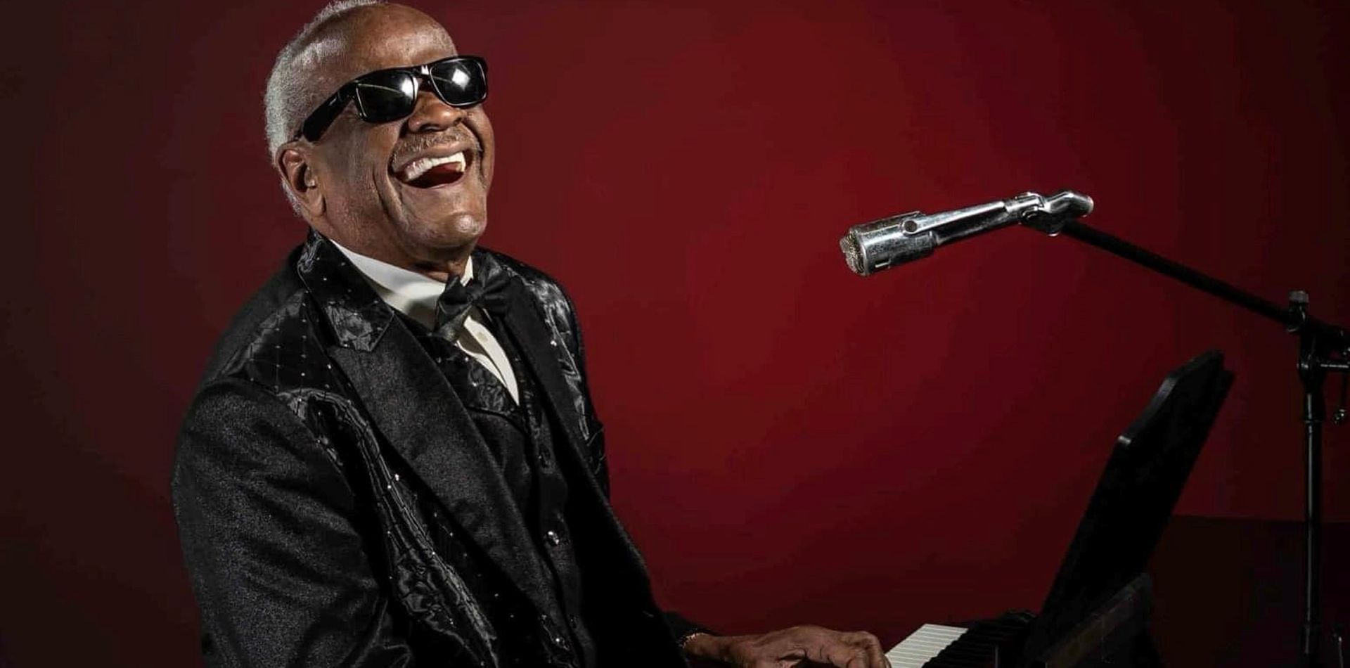 A man in a suit is playing a piano and singing into a microphone.