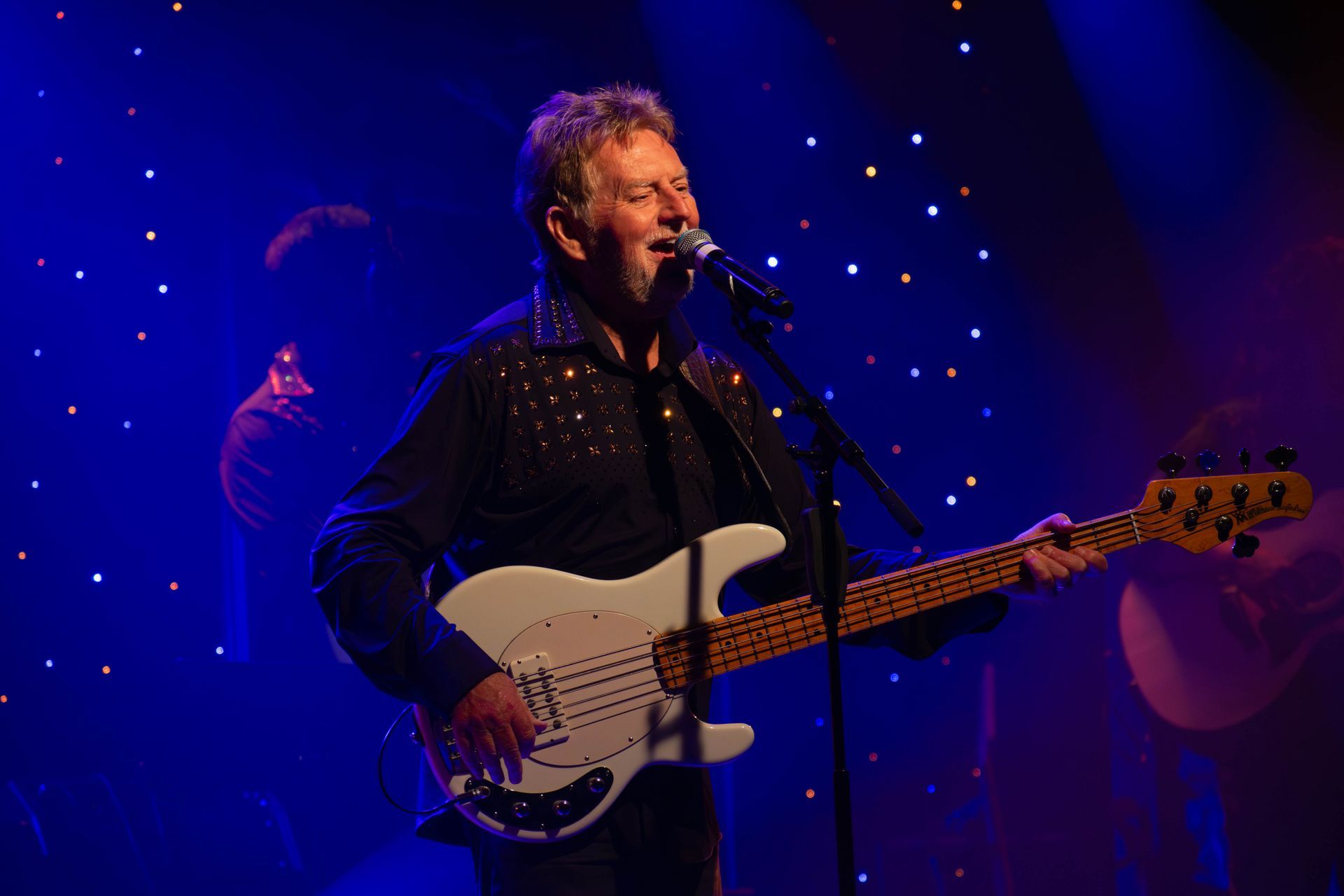 A man is playing a bass guitar and singing into a microphone on a stage.