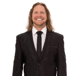 A man with long hair is wearing a suit and tie and smiling.