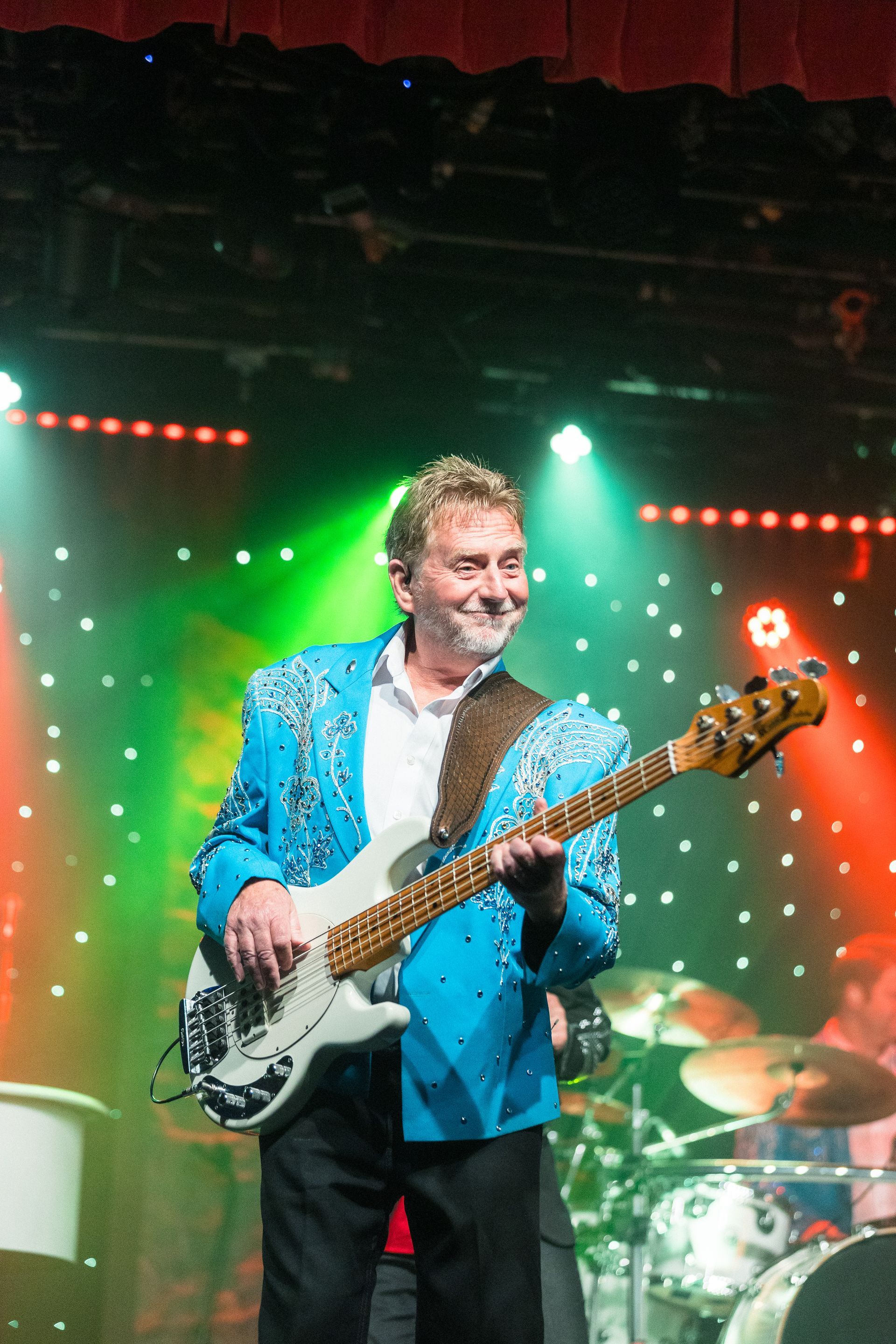 A man in a blue jacket is playing a guitar on a stage.