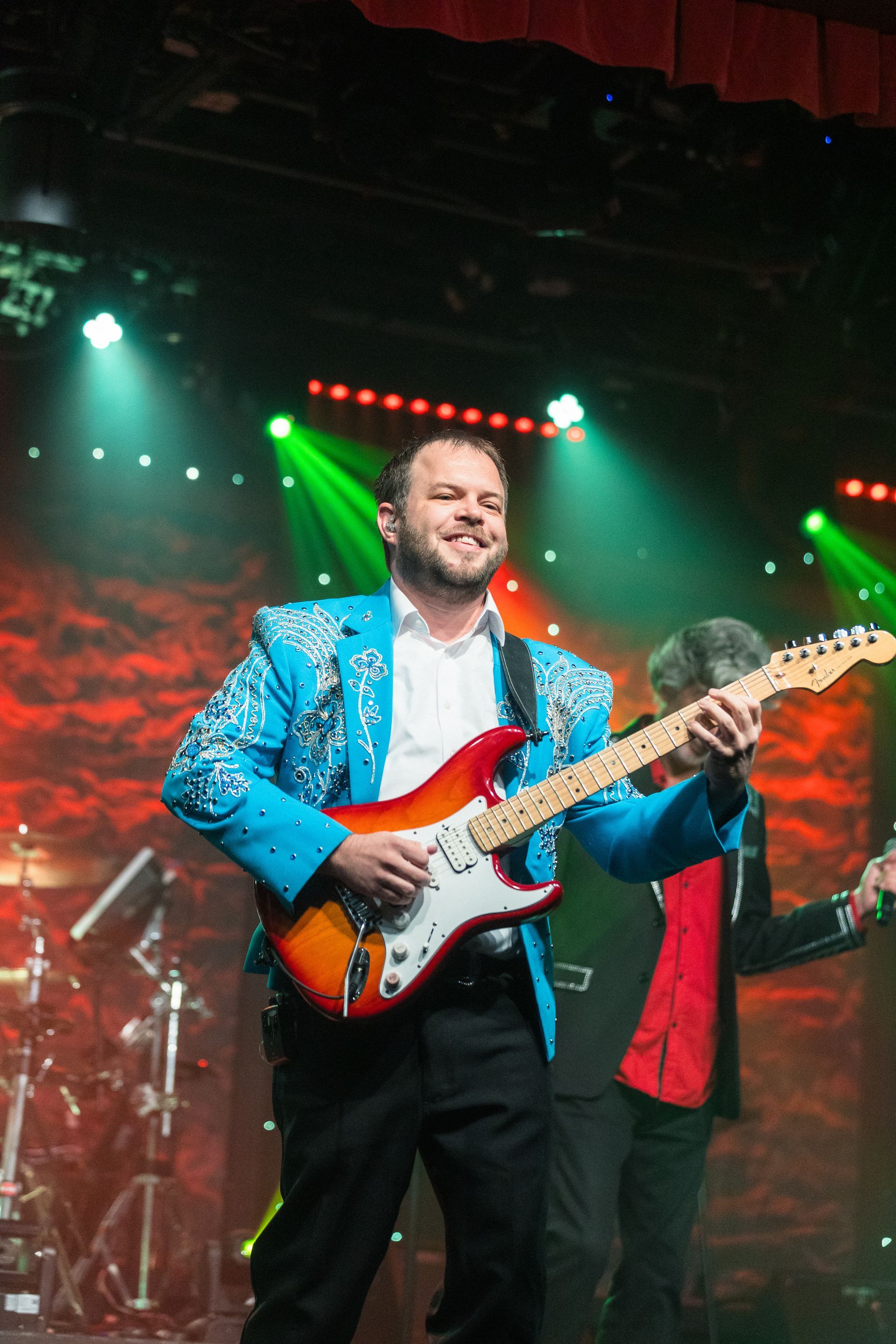 A man in a blue jacket is playing a guitar on stage