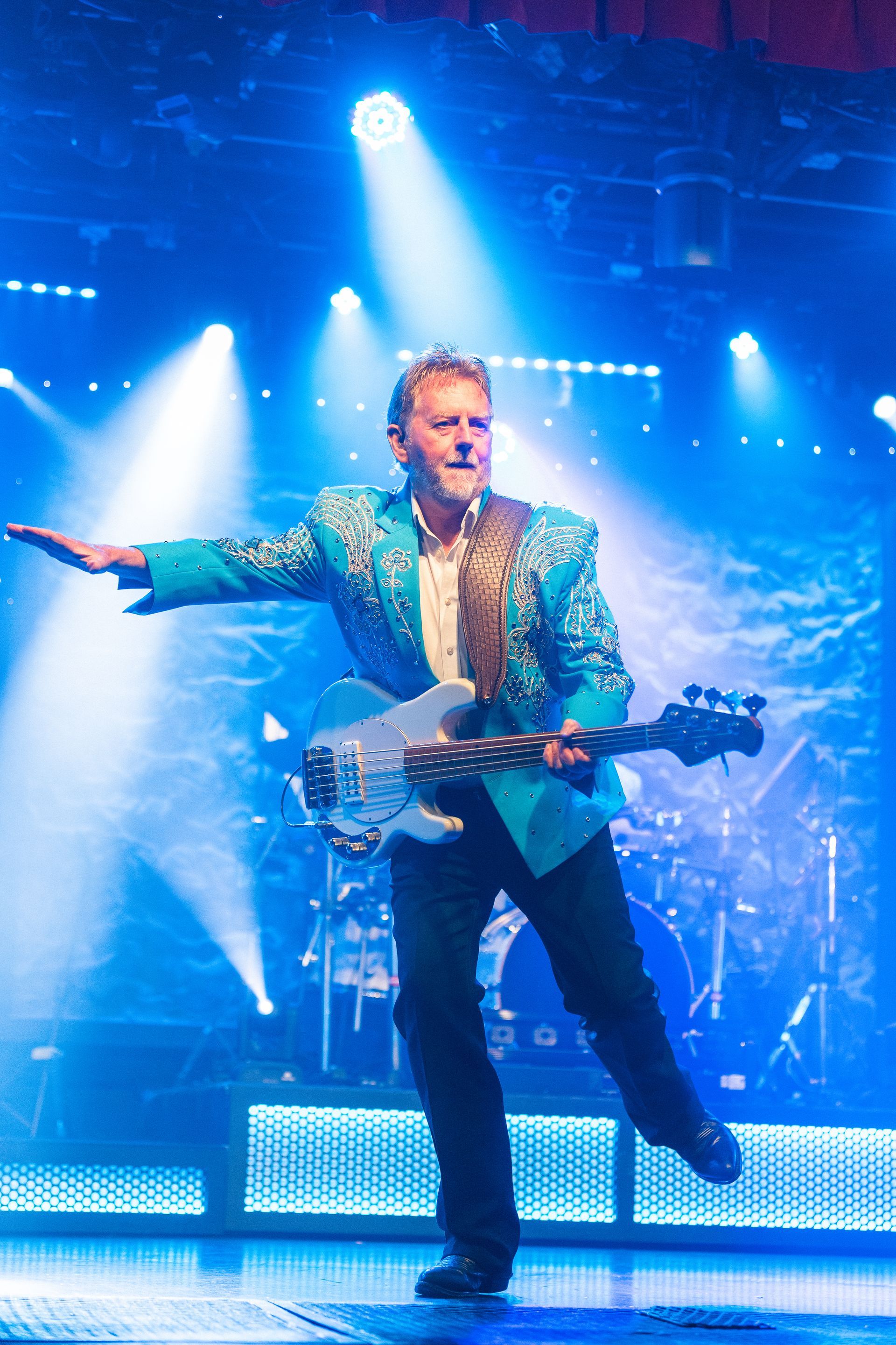 A man in a green jacket is playing a guitar on stage