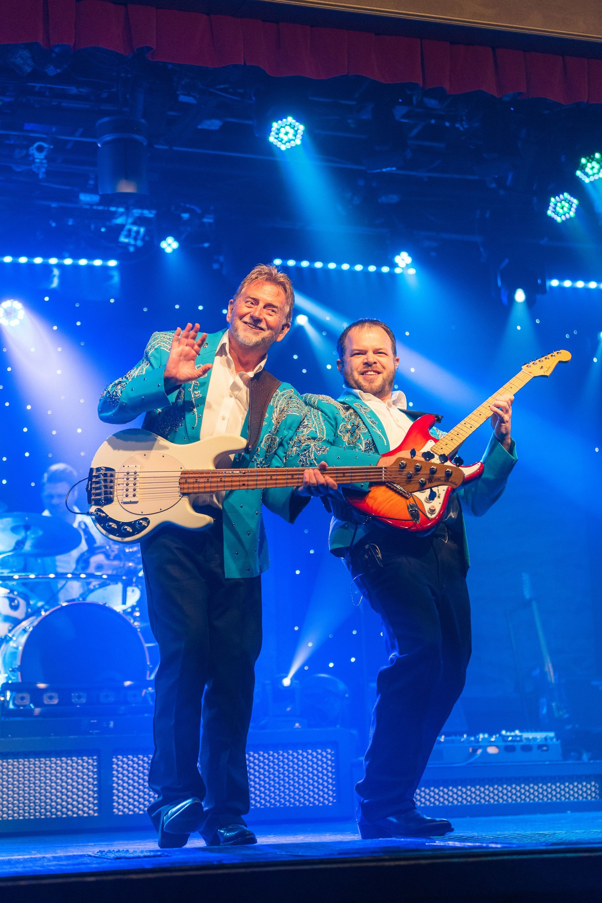 Two men are standing on a stage holding guitars.