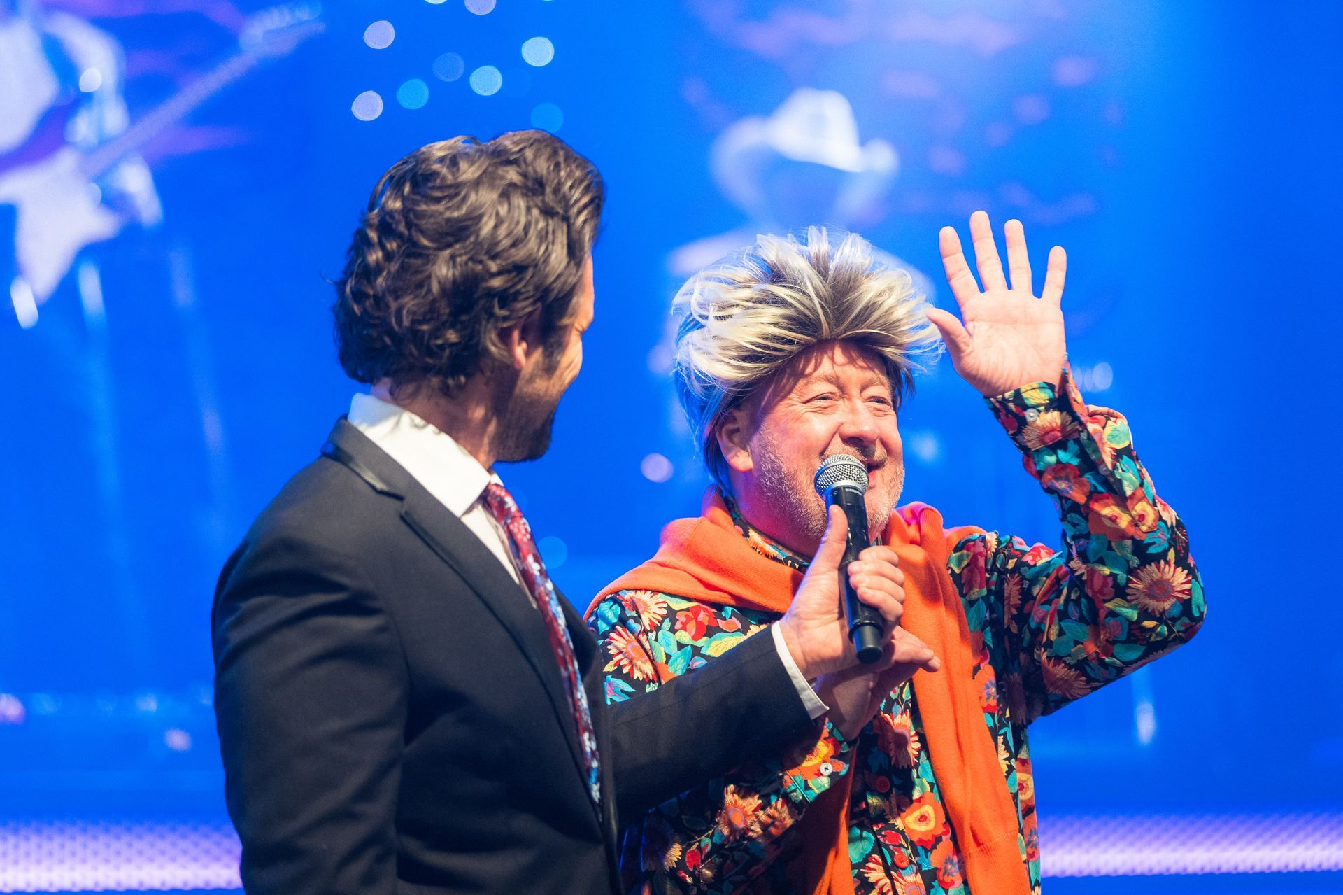 Two men are standing next to each other on a stage and one of them is holding a microphone.