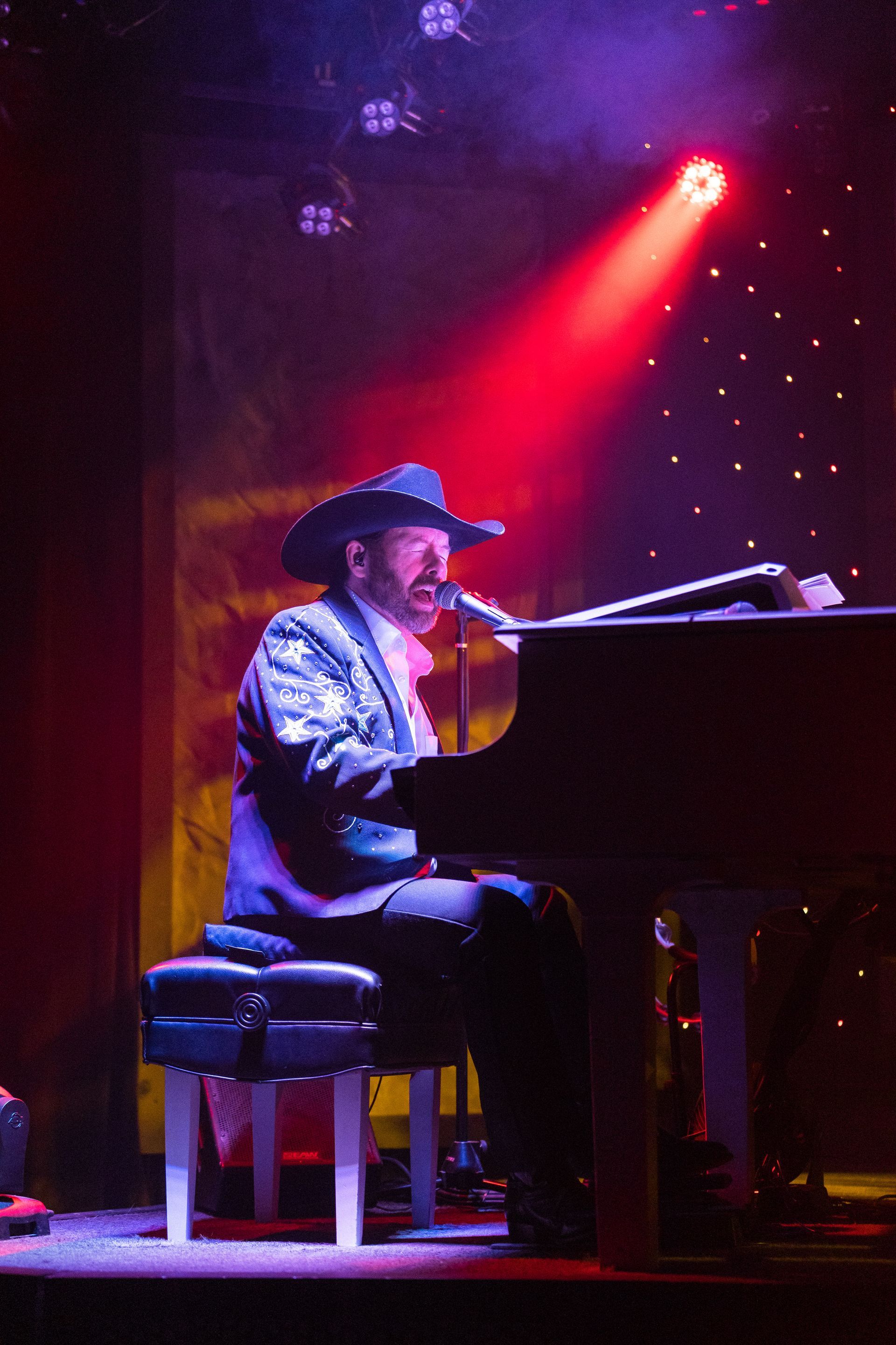 A man in a cowboy hat is playing a piano on a stage.