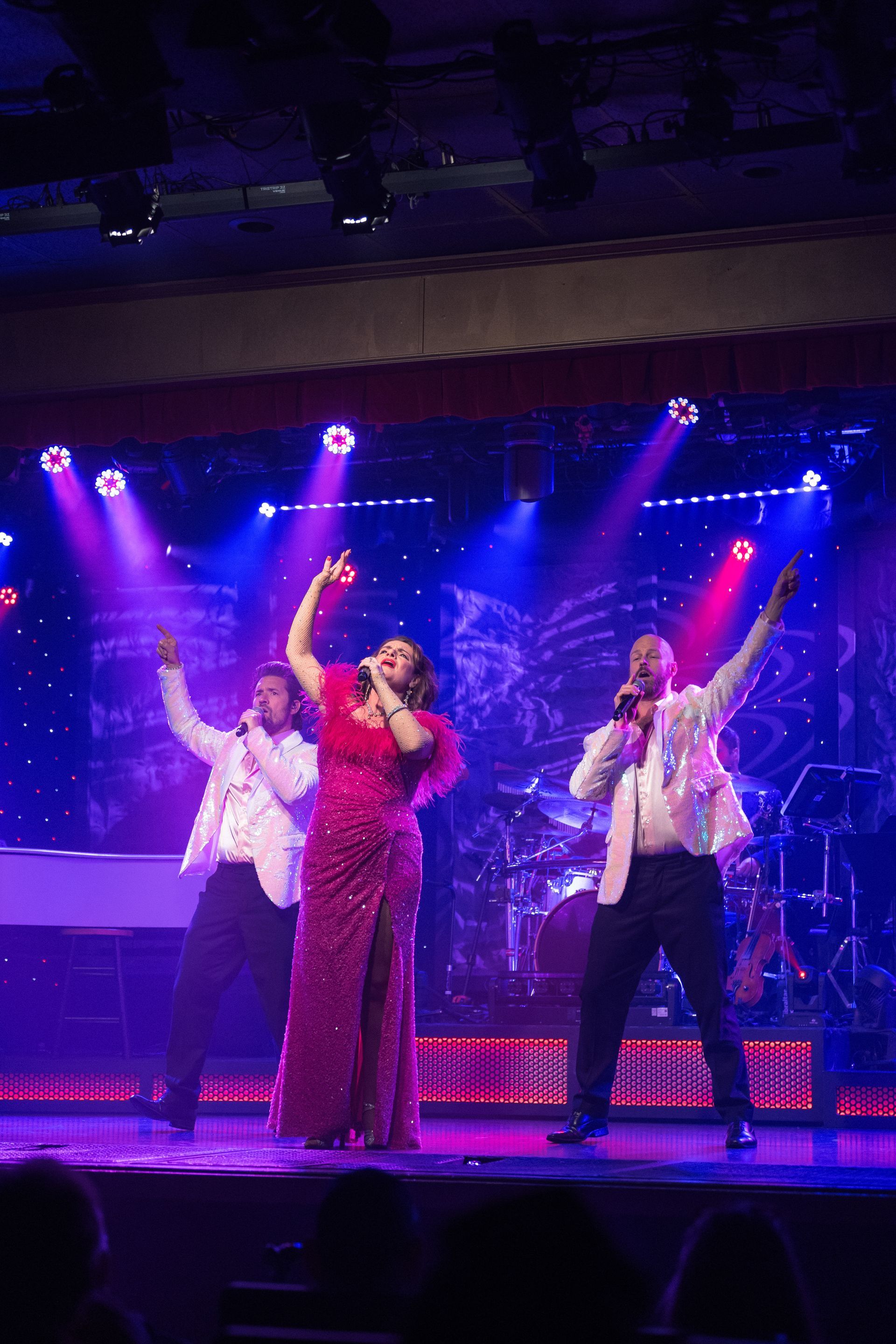 A group of people are standing on a stage singing into microphones.
