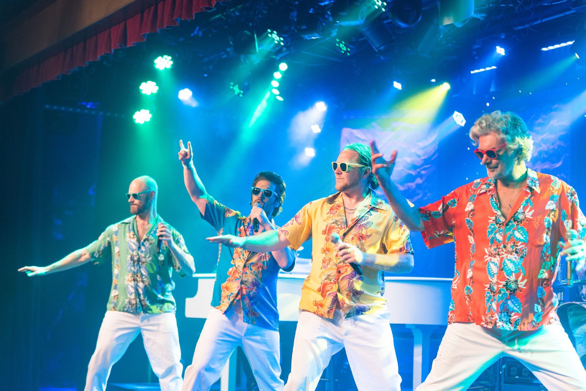 A group of men in hawaiian shirts are dancing on a stage.