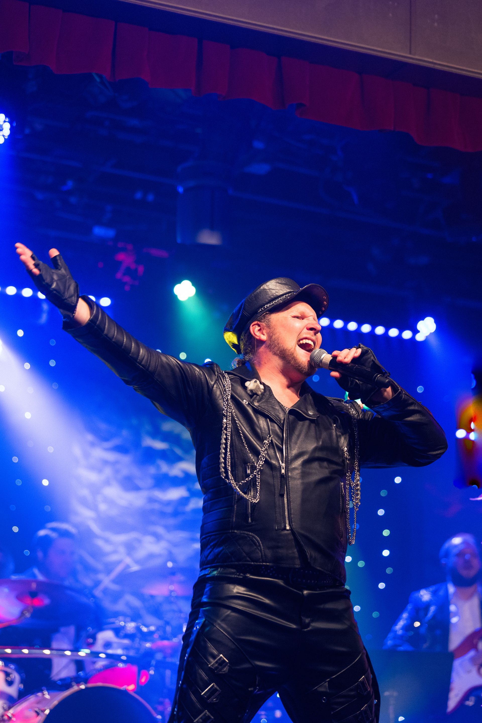 A man in a leather jacket is singing into a microphone on a stage.