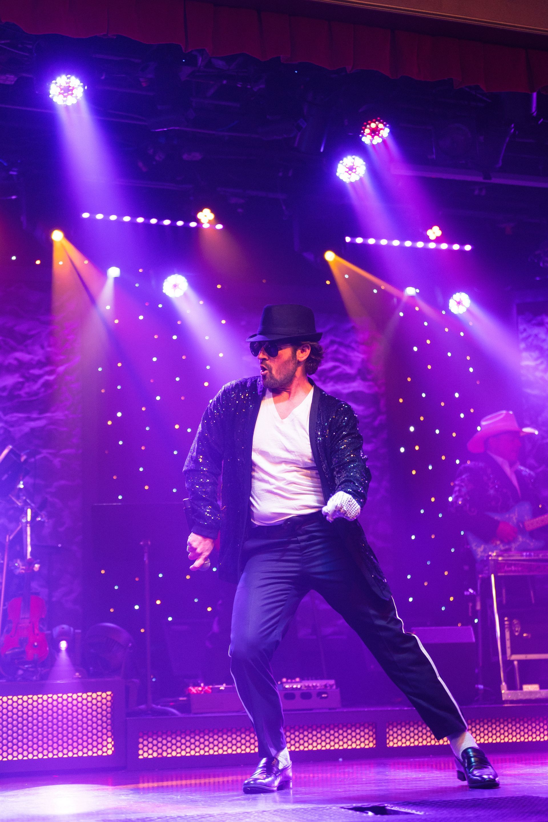A man in a top hat is dancing on a stage with purple lights