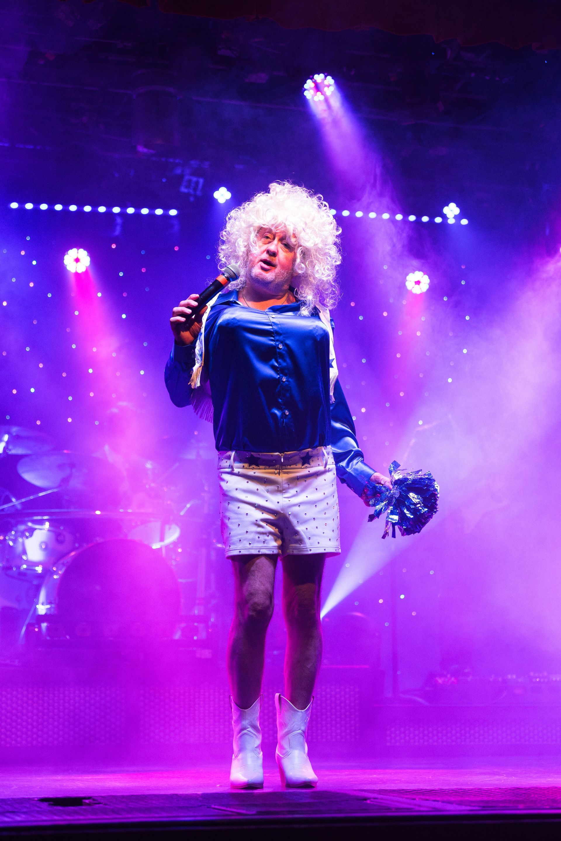 A man in a wig is singing into a microphone on a stage.