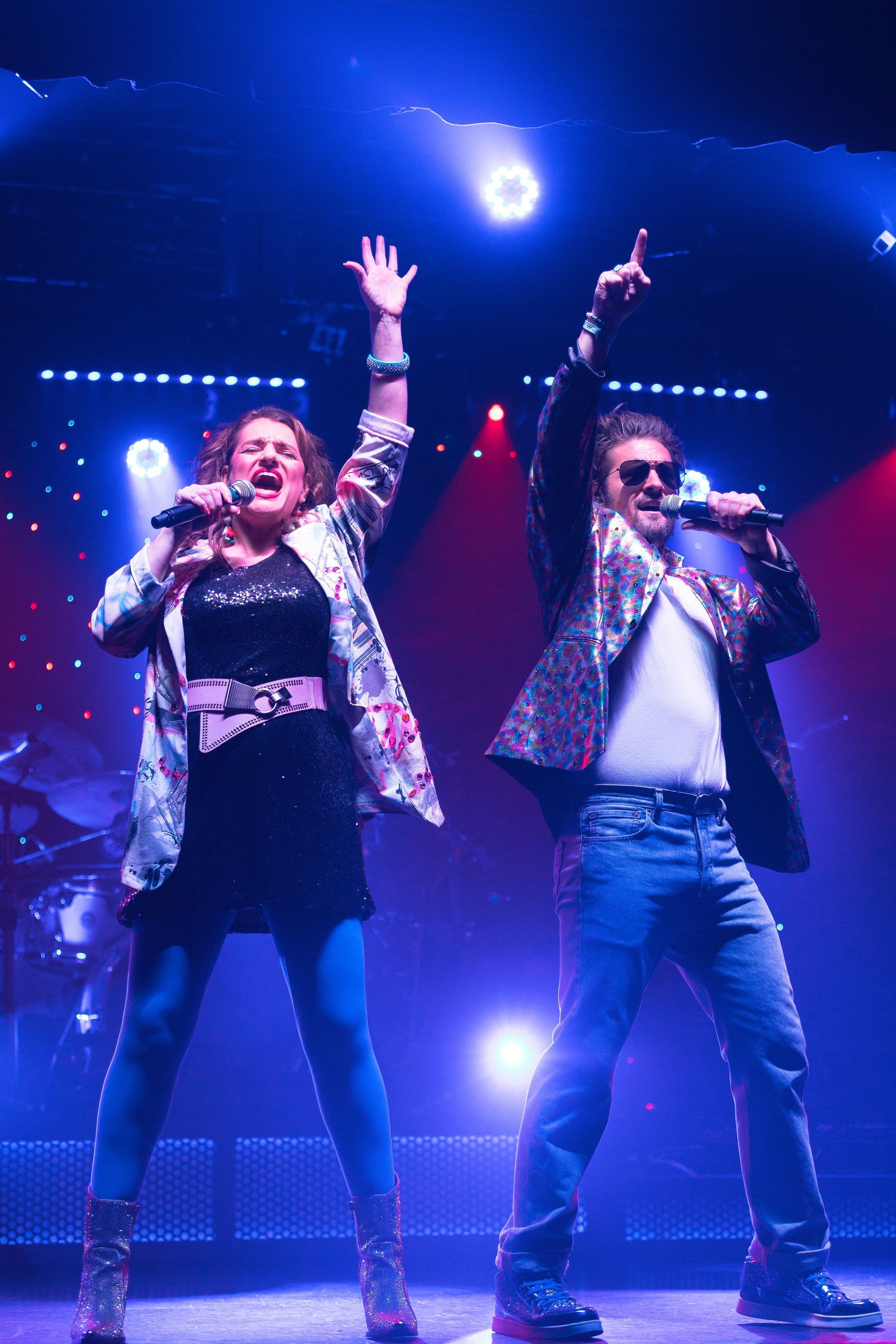 A man and a woman are singing into microphones on a stage.