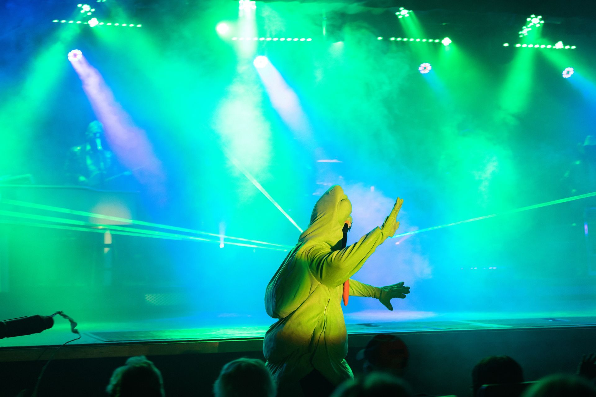 A person in a yellow jacket is standing on a stage with green lights behind them.