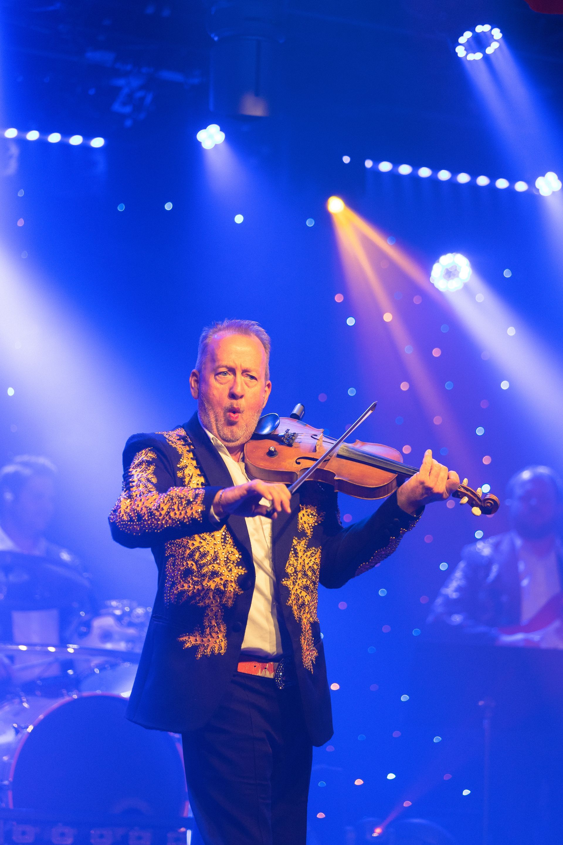 A man in a suit is playing a violin on a stage.