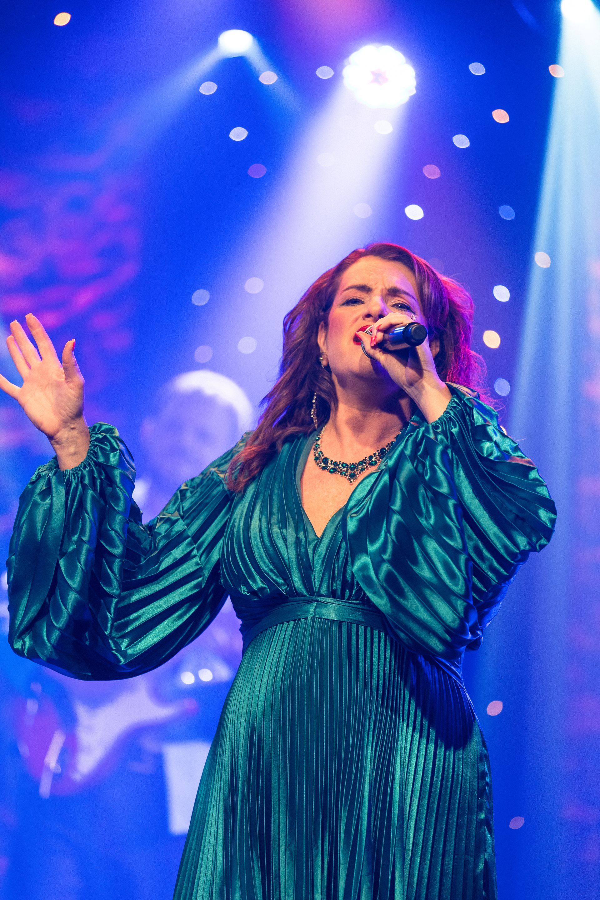A woman in a green dress is singing into a microphone on a stage.