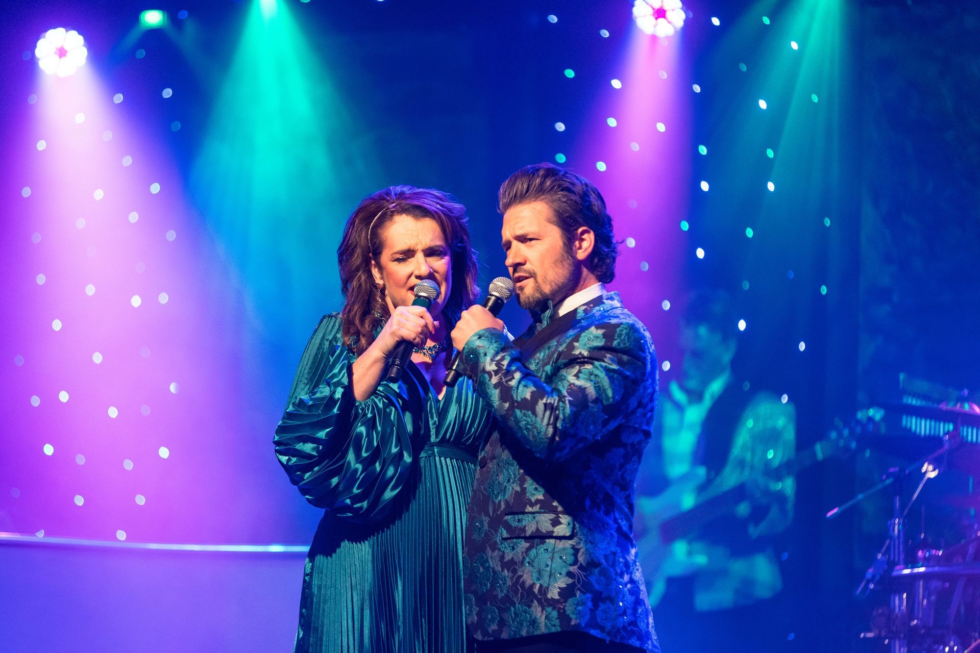 A man and a woman are singing into microphones on a stage.