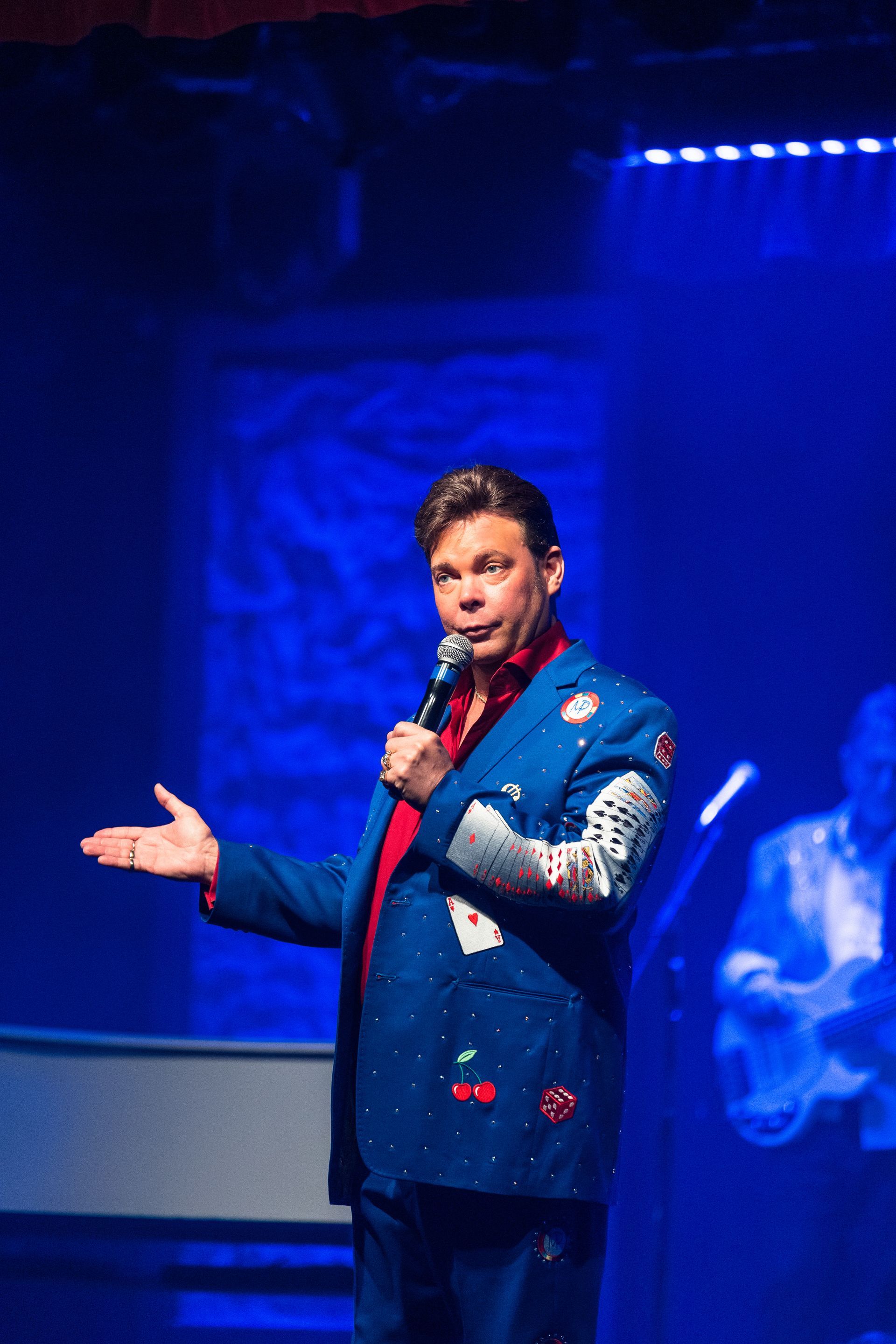 A man in a blue suit is holding a microphone on a stage.