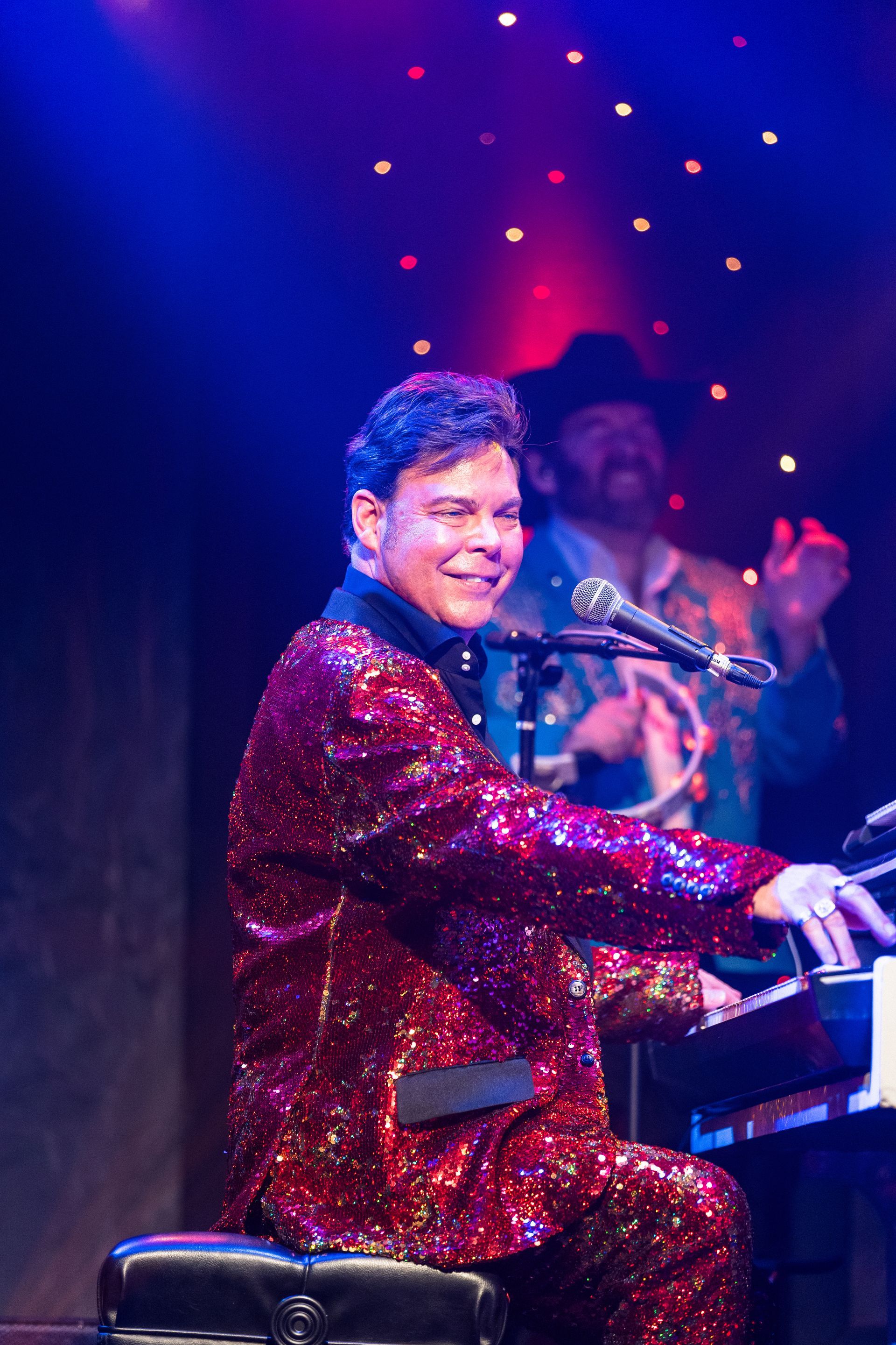 A man in a red suit is playing a piano on a stage.