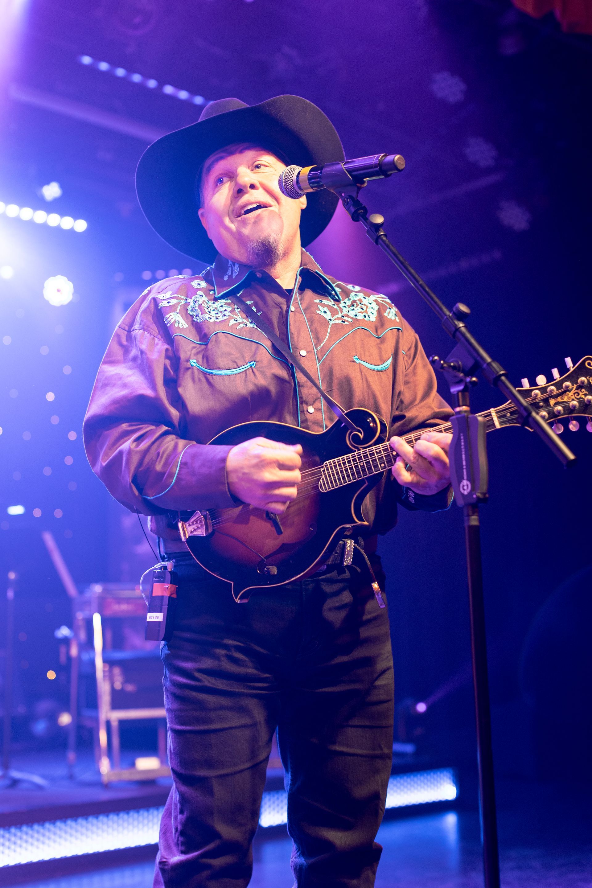 A man in a cowboy hat is playing a guitar and singing into a microphone.