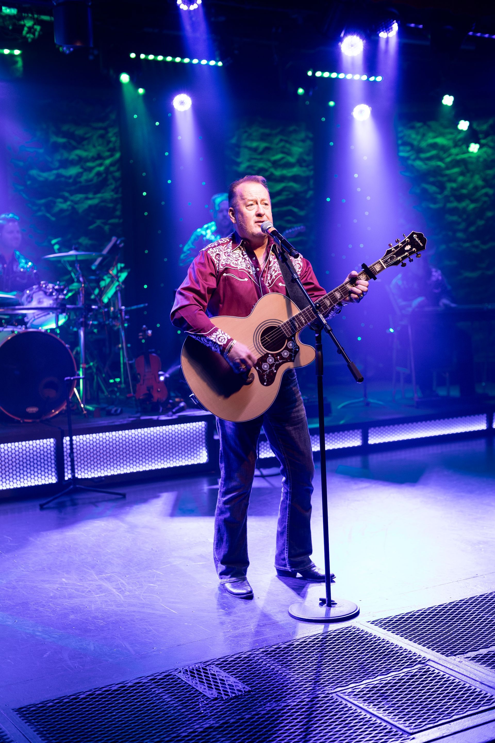 A man is playing a guitar and singing into a microphone on a stage.