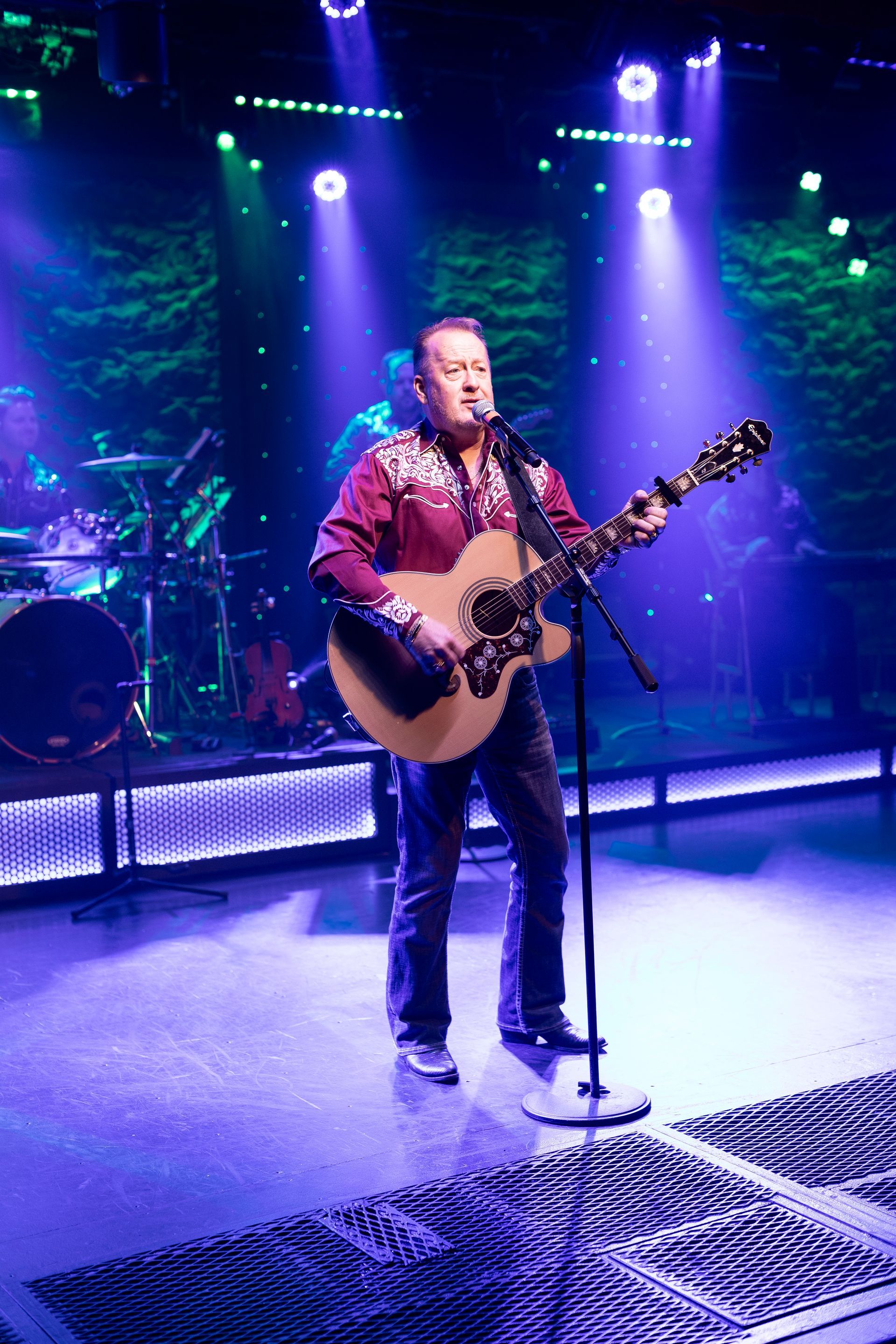 A man is playing a guitar and singing into a microphone on a stage.