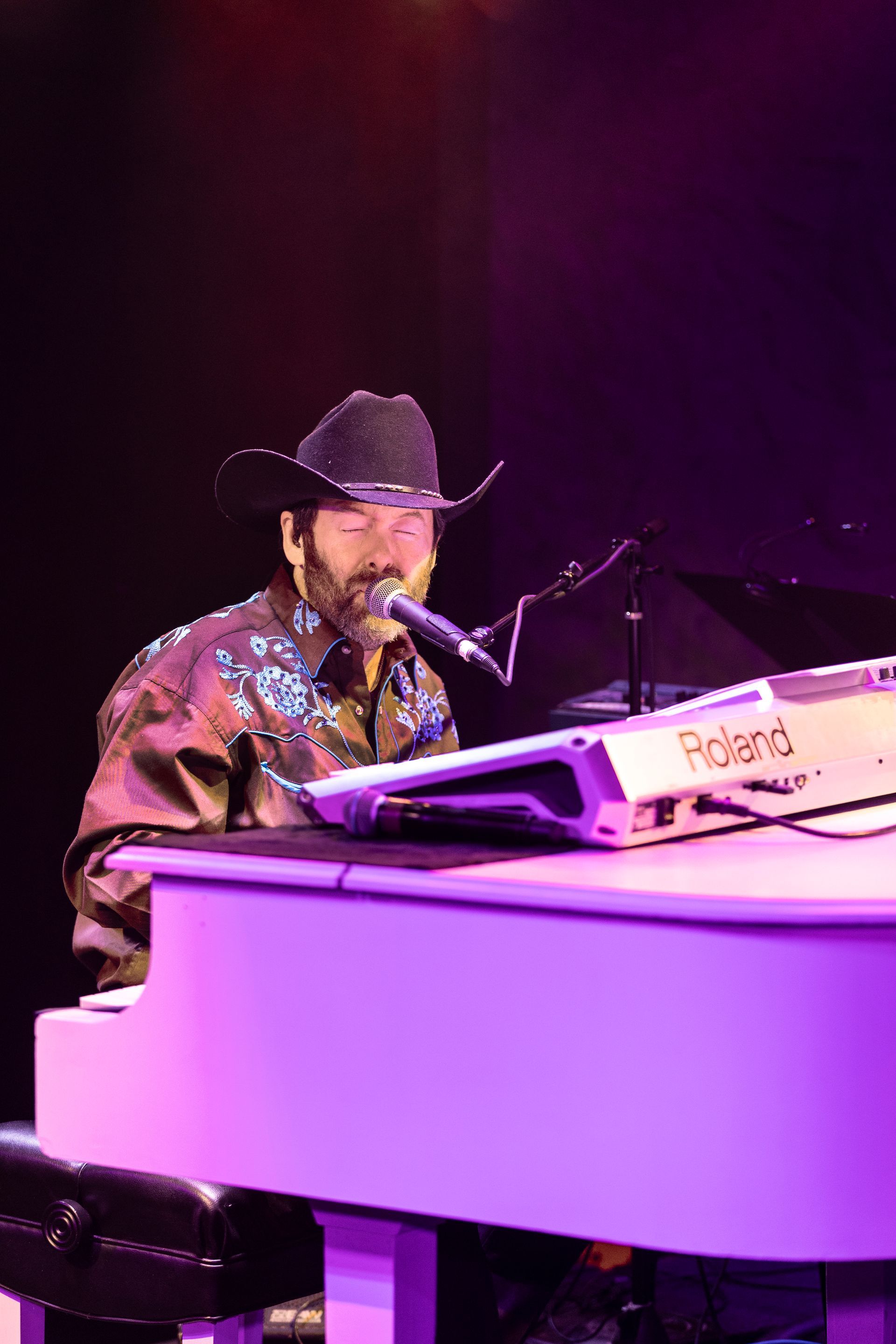 A man in a cowboy hat is playing a piano and singing into a microphone.