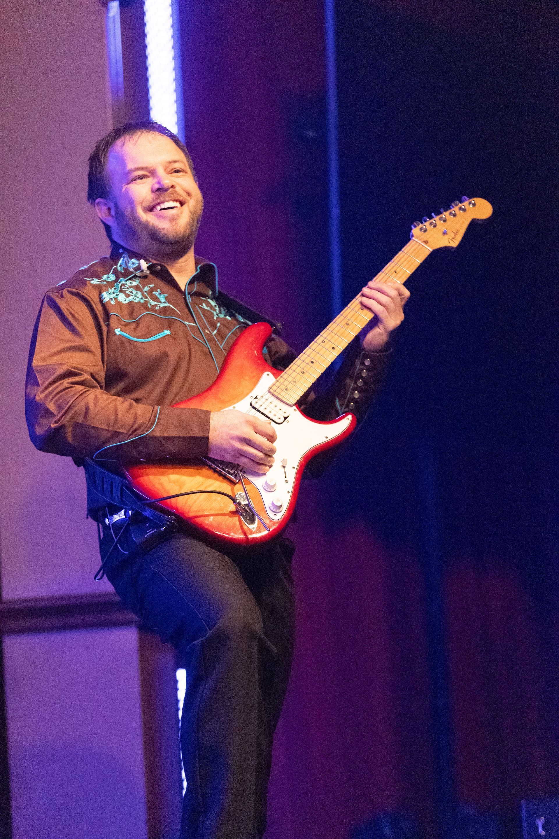 A man in a brown shirt is playing an electric guitar