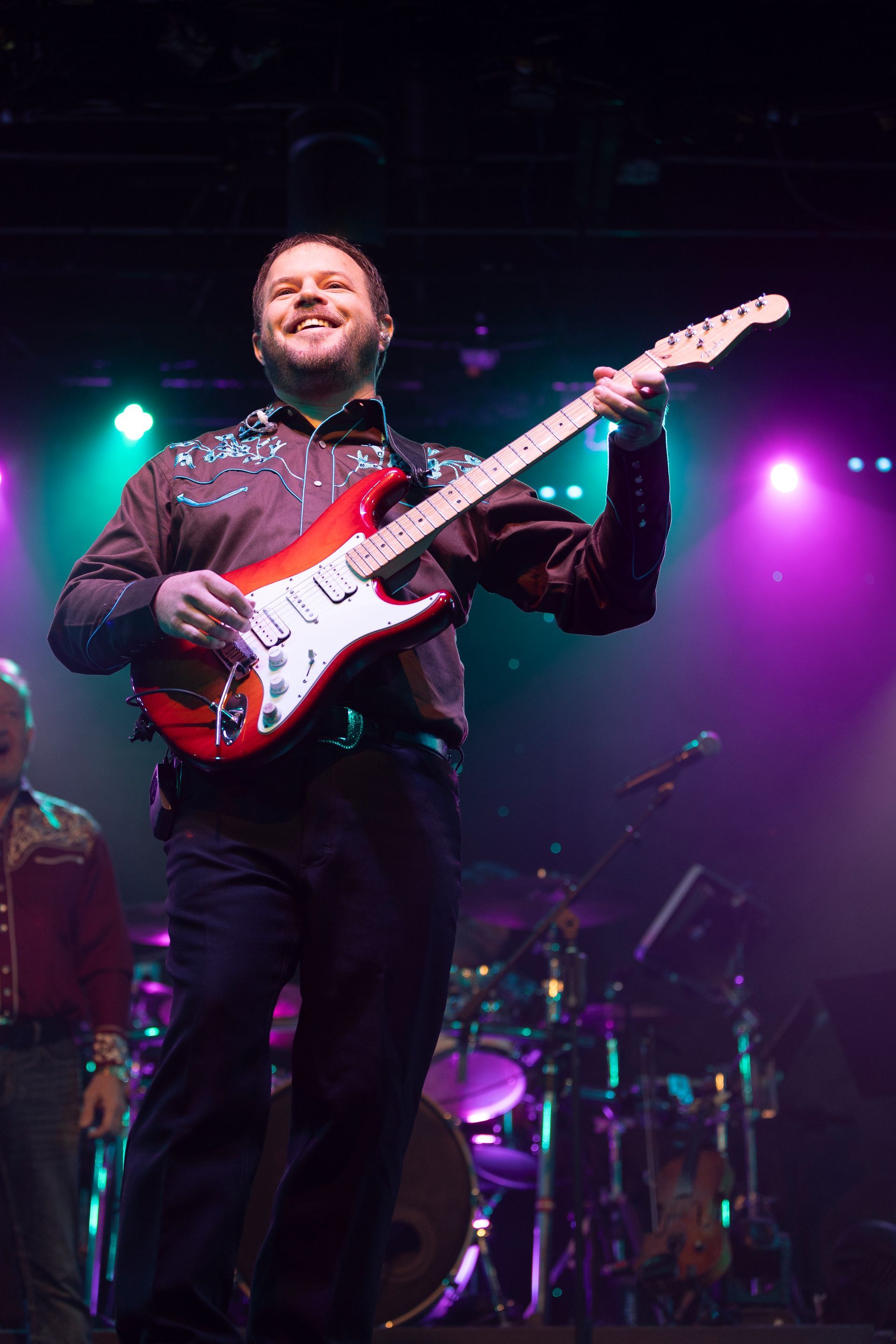 A man is playing a red electric guitar on a stage.