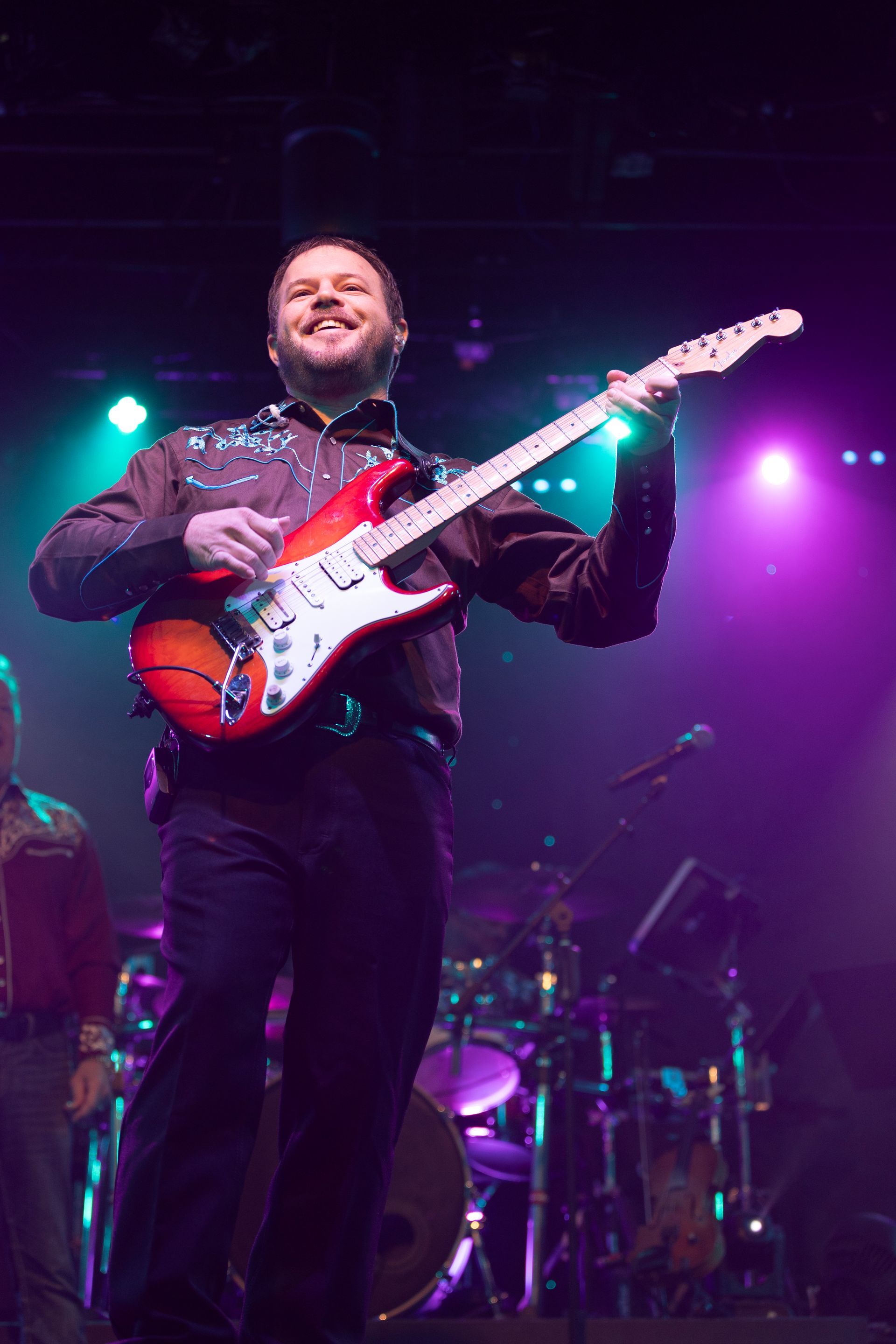 A man is playing a guitar on a stage with purple lights behind him