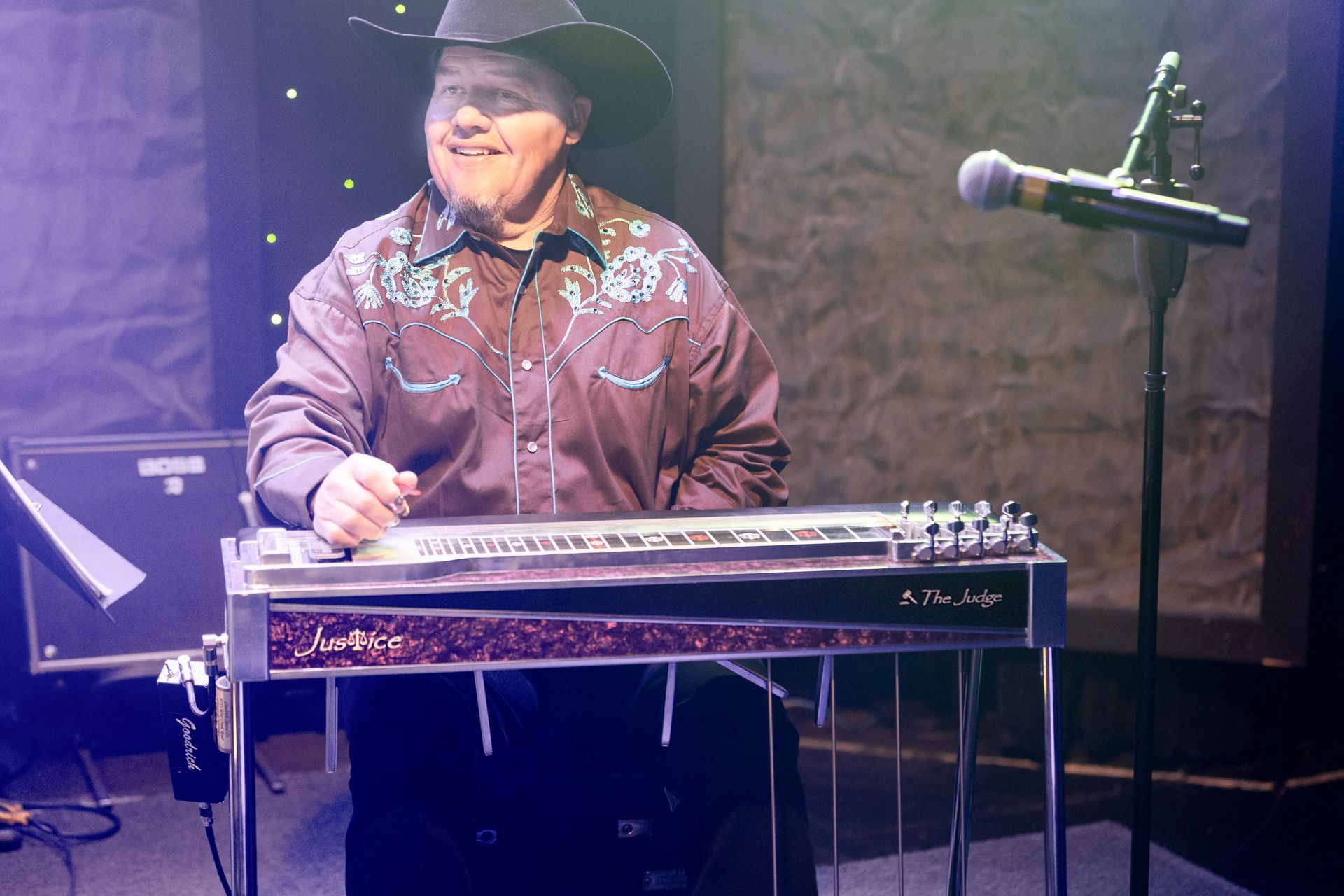 A man in a cowboy hat is playing a guitar in front of a microphone.