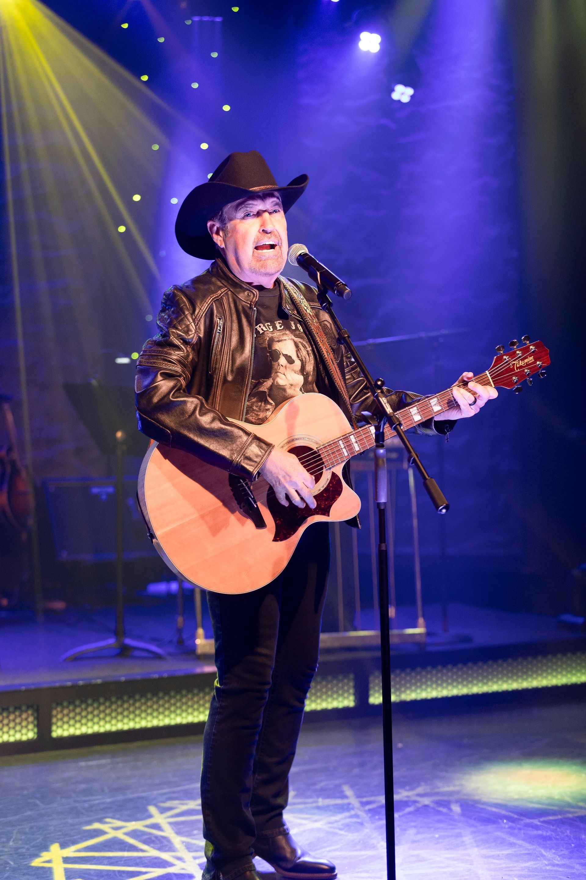 A man in a cowboy hat is playing a guitar and singing into a microphone on a stage.