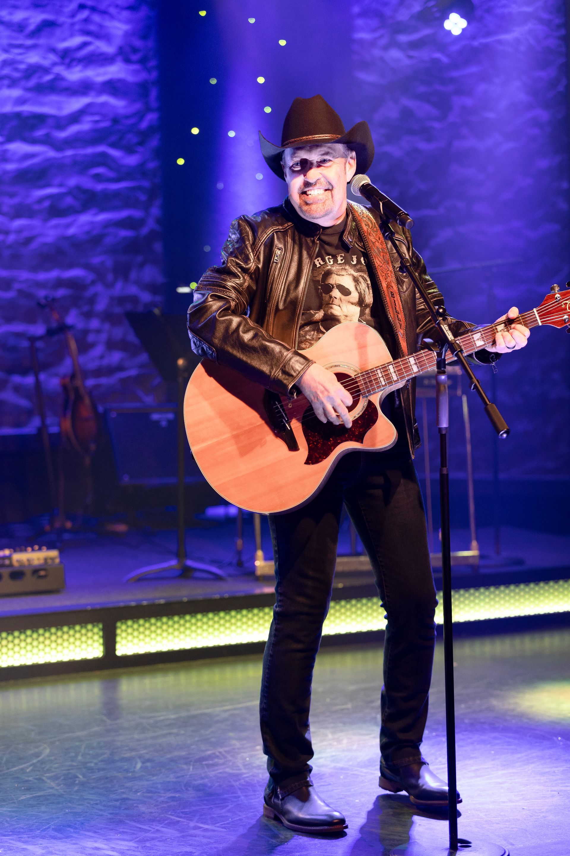 A man in a cowboy hat is playing a guitar and singing into a microphone.