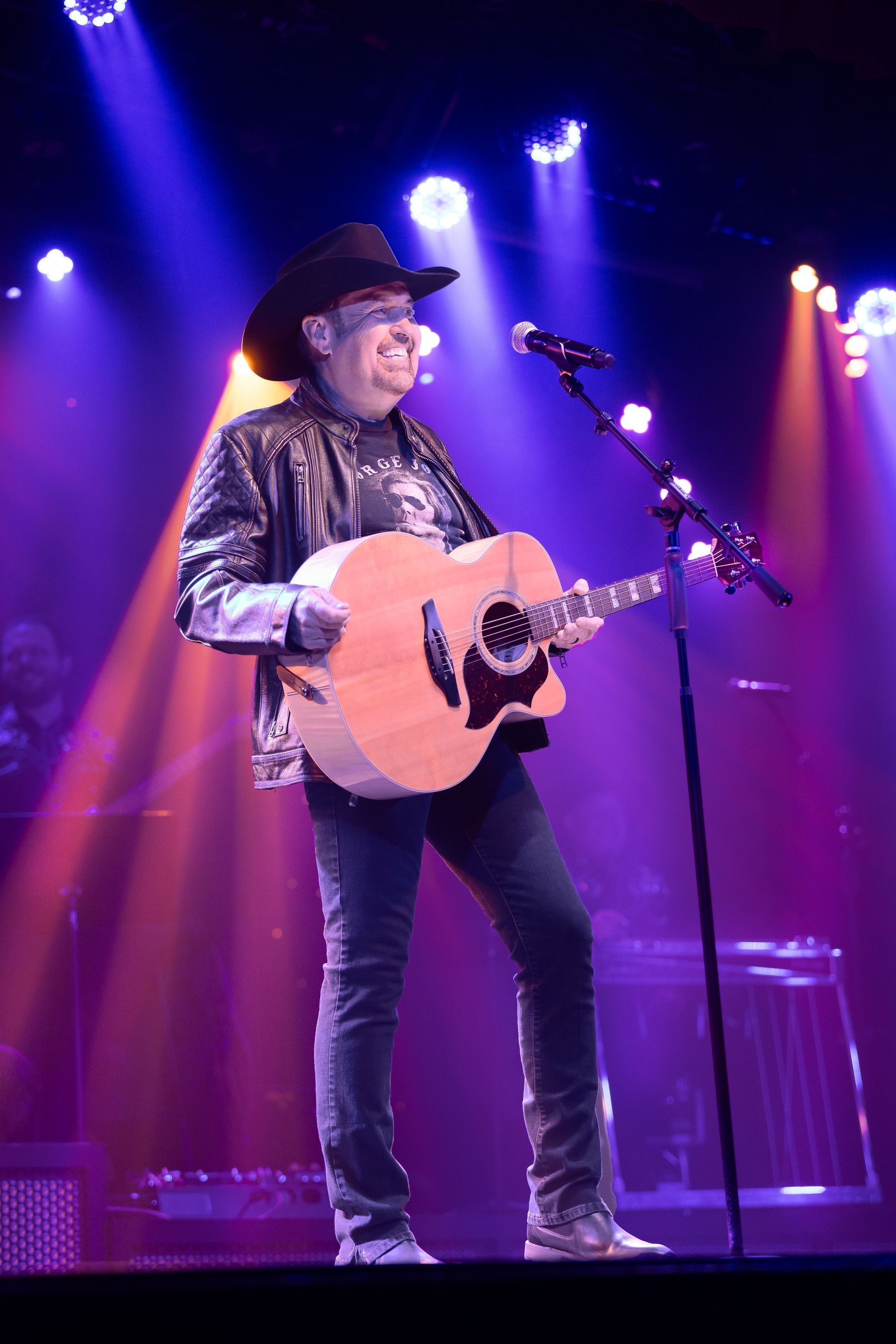 A man in a cowboy hat is playing a guitar and singing into a microphone on a stage.