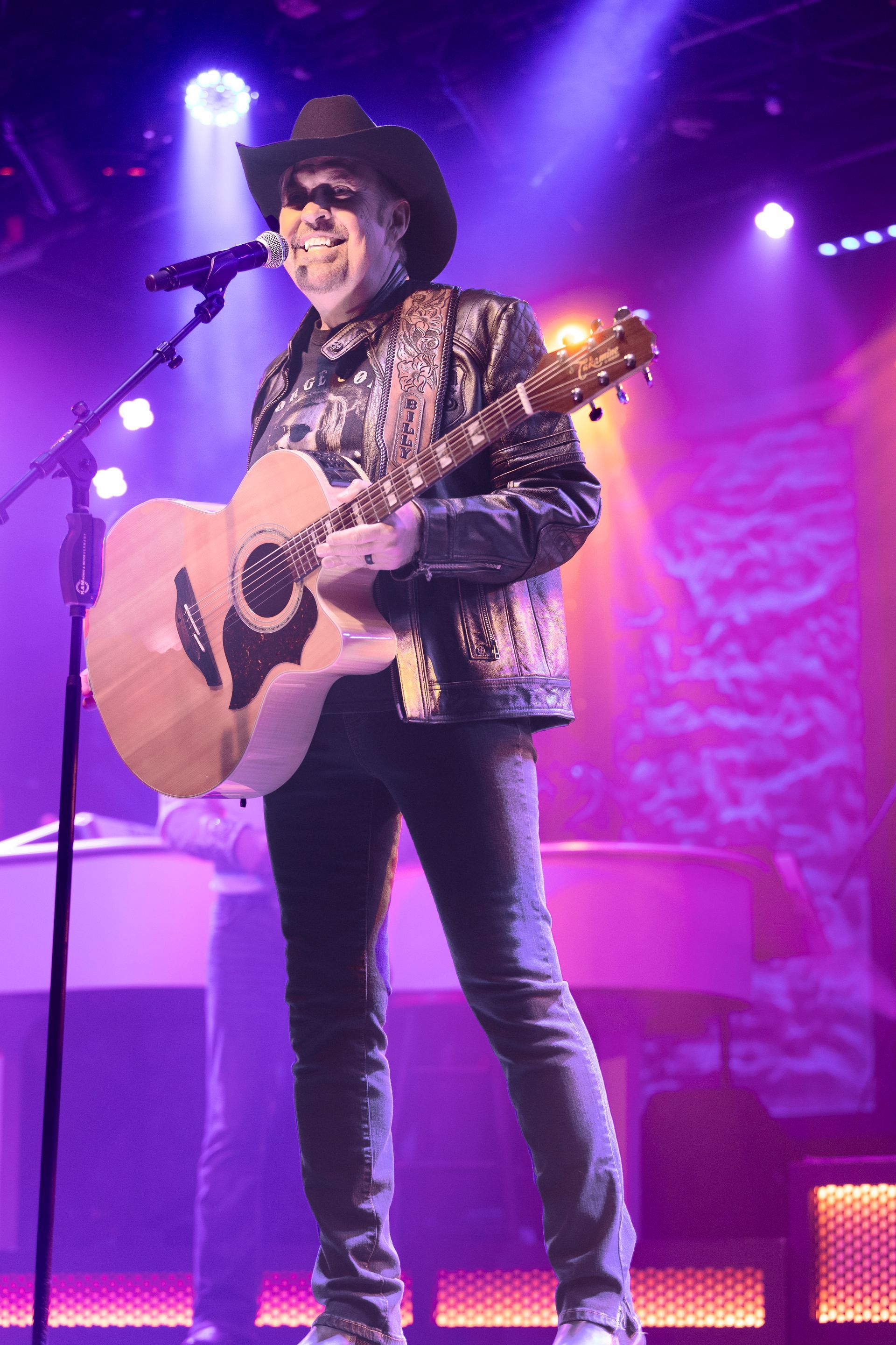 A man in a cowboy hat is playing a guitar and singing into a microphone on a stage.
