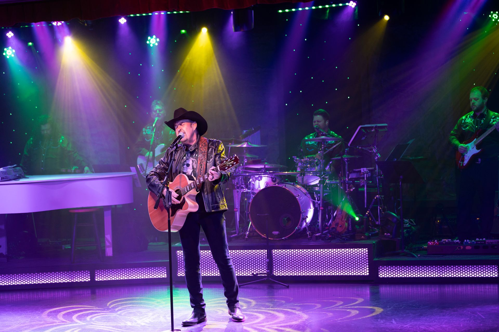 A man is singing into a microphone on a stage while playing a guitar.