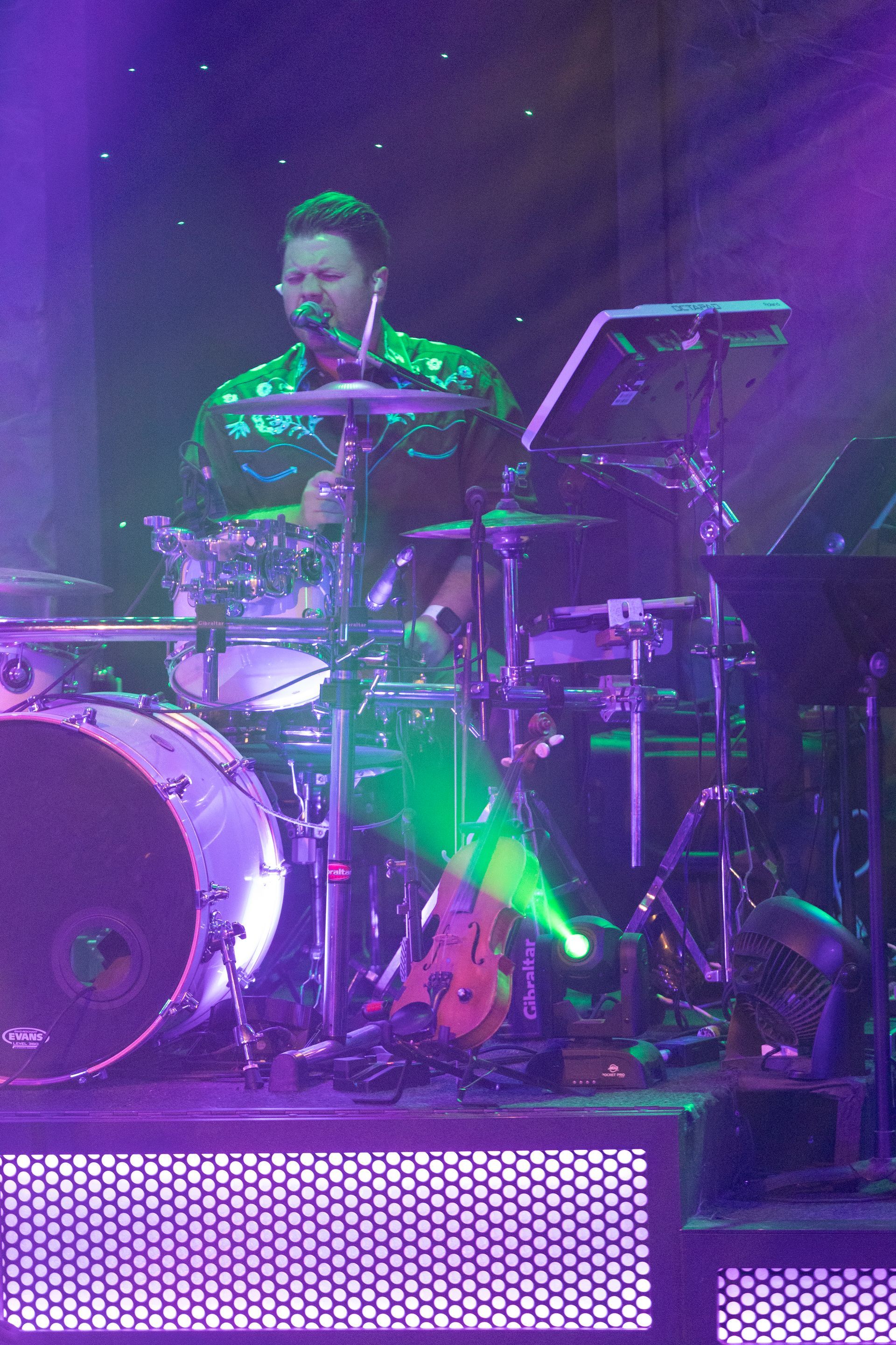 A man playing drums on a stage with purple lights