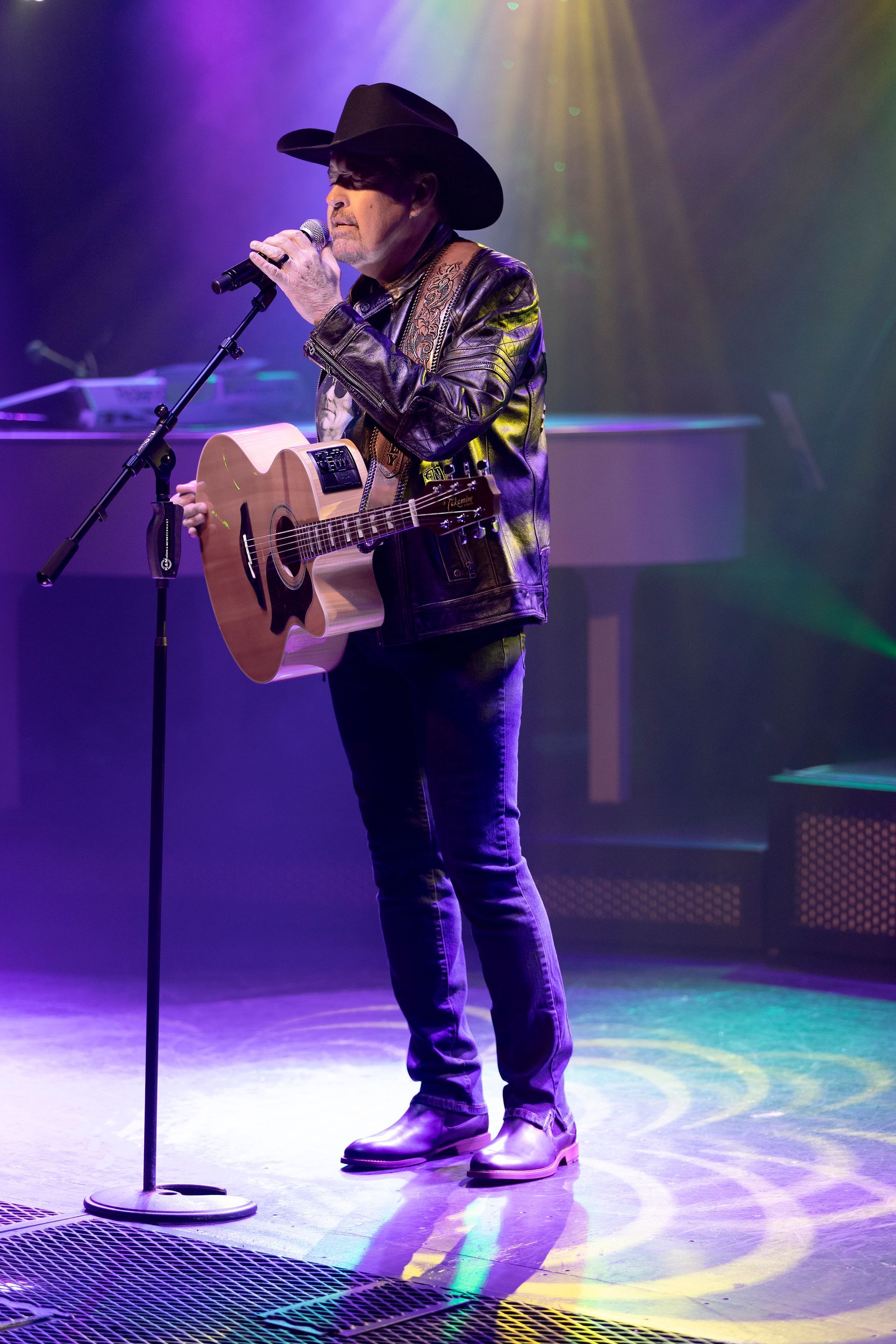 A man in a cowboy hat is singing into a microphone while playing a guitar on a stage.