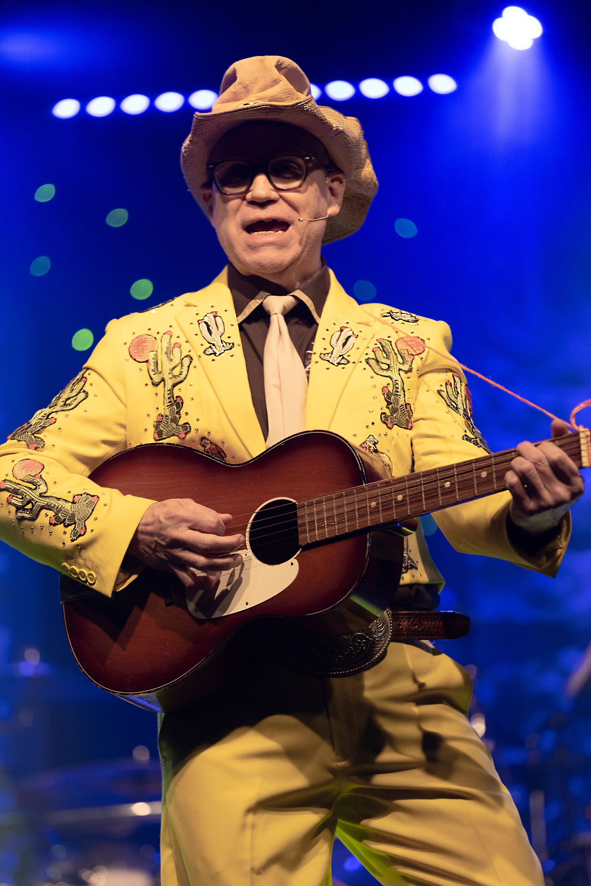 A man in a yellow suit is playing a guitar on stage
