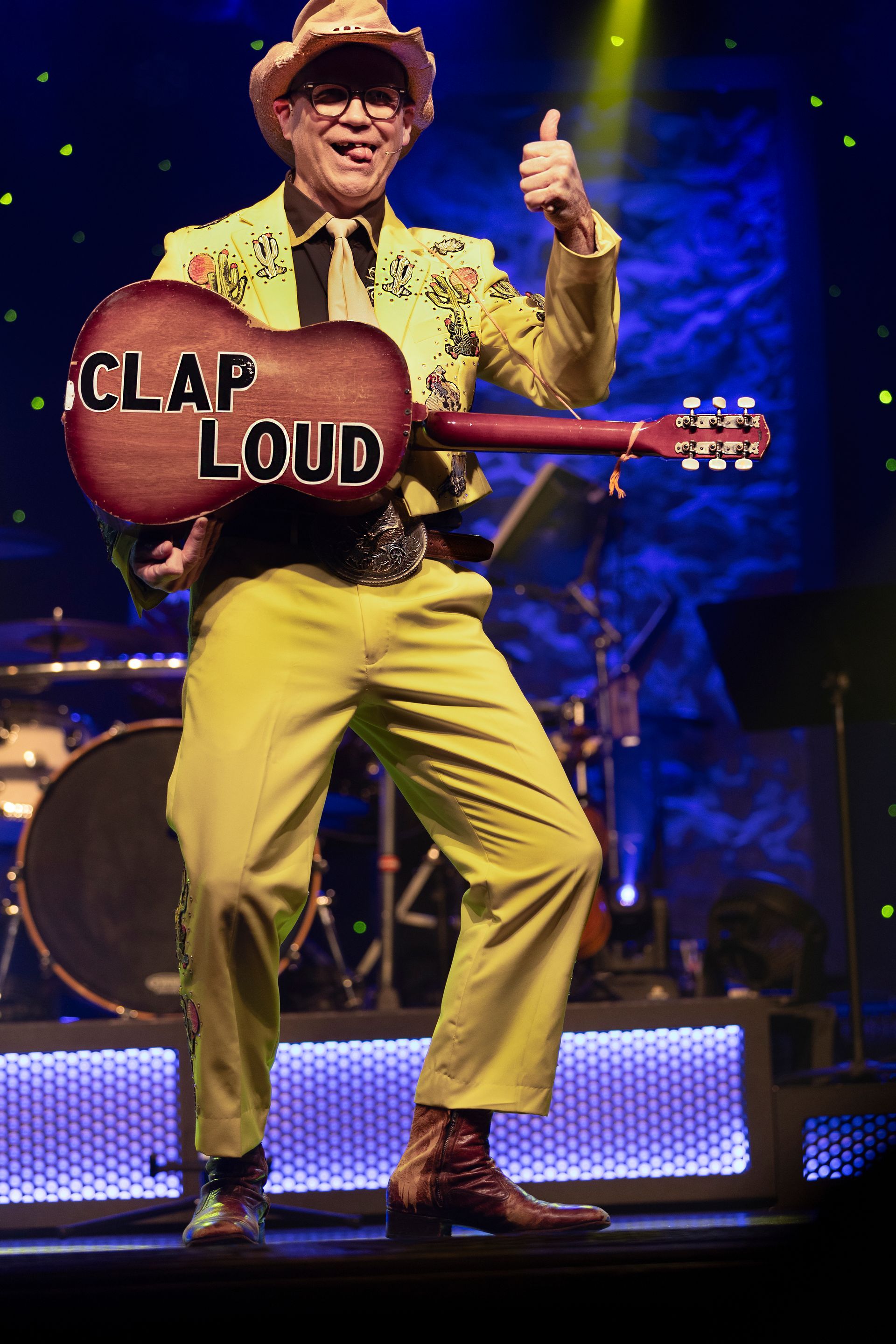 A man in a yellow suit is holding a guitar that says clap loud