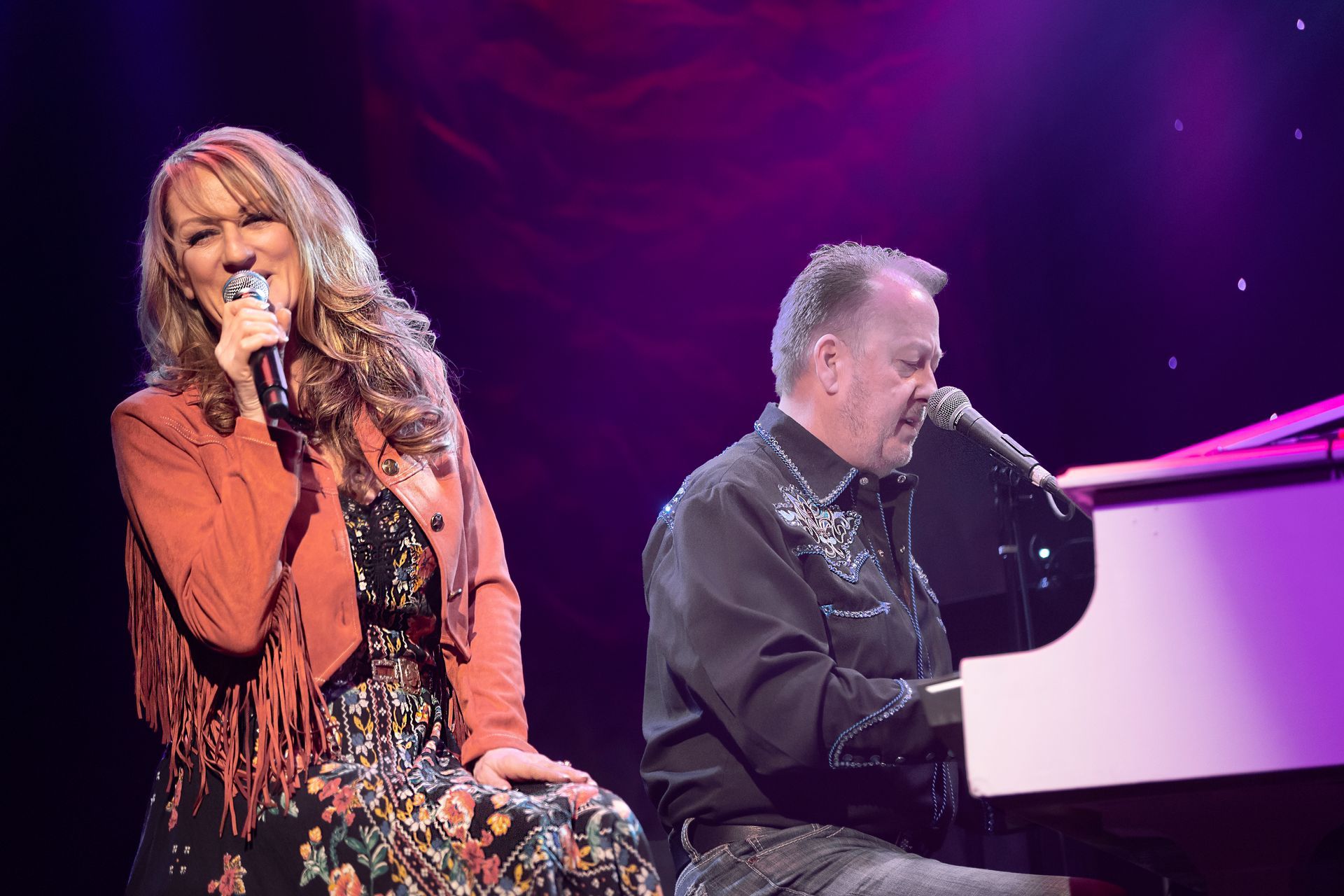 A woman is singing next to a man playing a piano on a stage.
