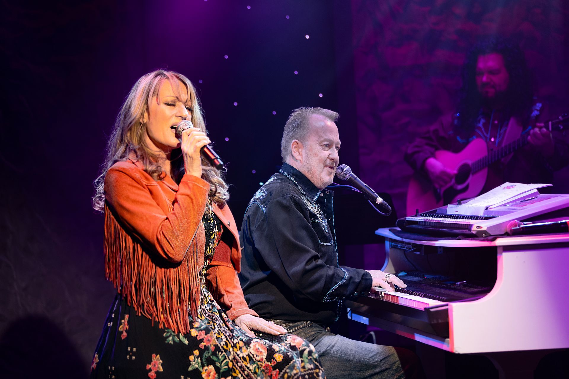 A woman is singing next to a man playing a piano on a stage.