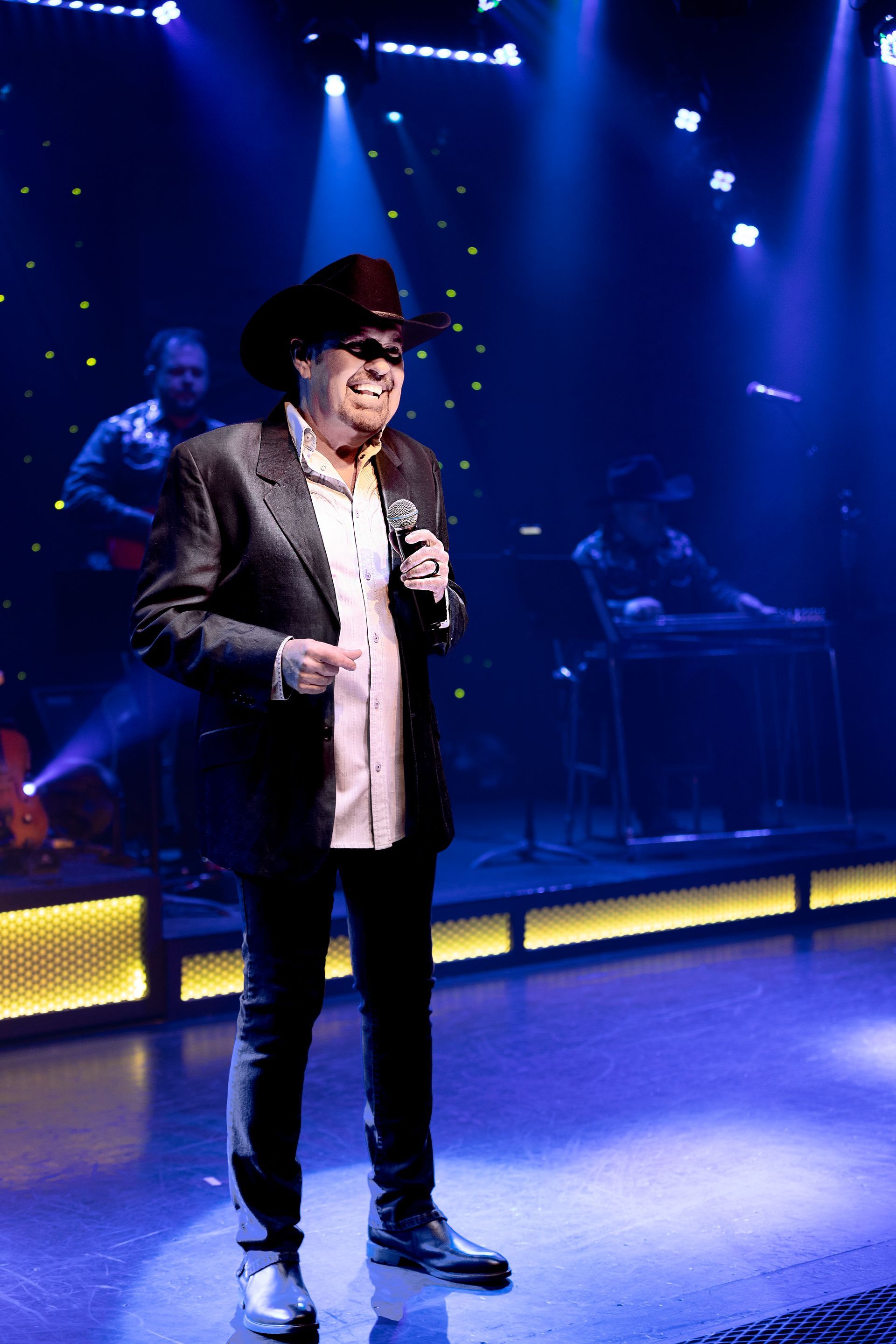 A man in a cowboy hat is singing into a microphone on a stage.